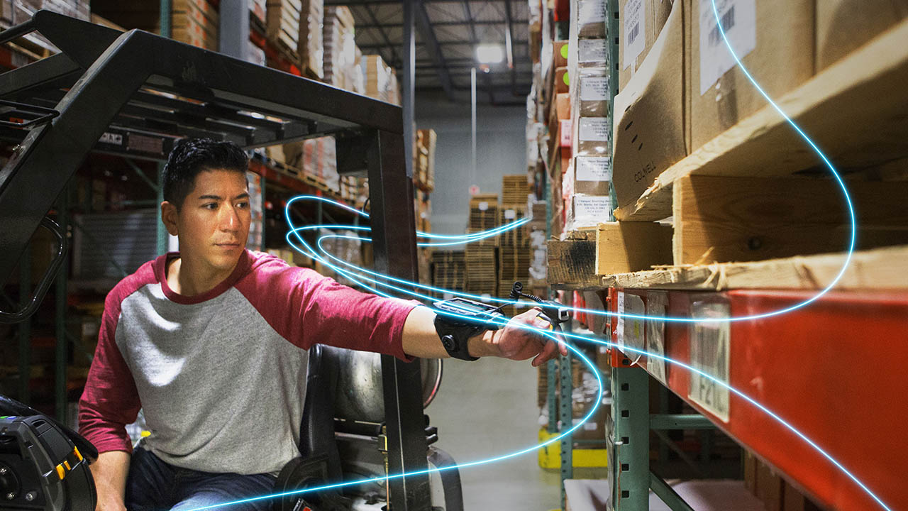 A warehouse associate uses wearable technology to collect data from shelved items