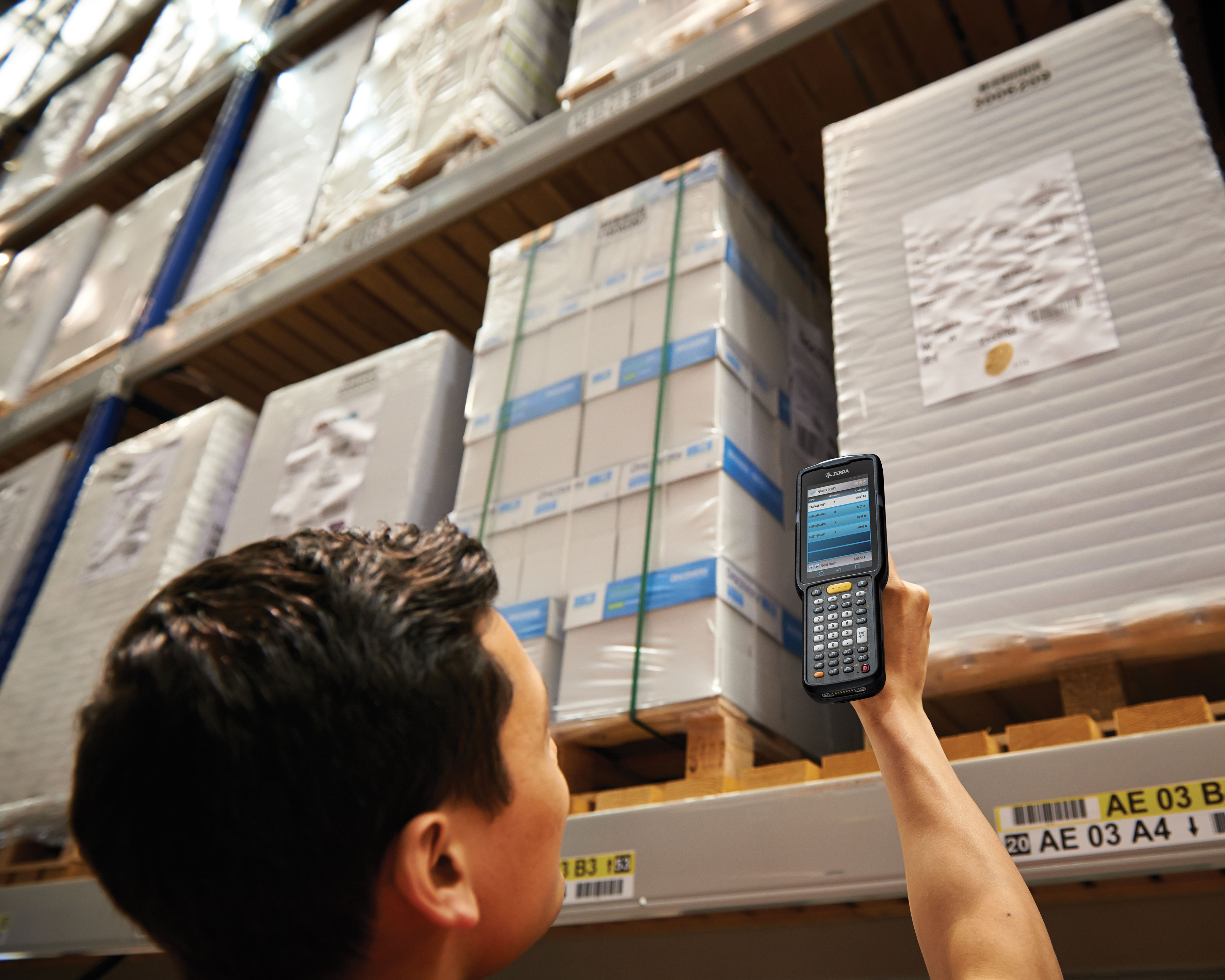 Warehouse worker uses Zebra MC3300 handheld computer gun pistol for long range scanning of boxes on shelves above