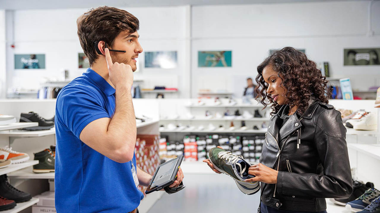 A retail associate uses a Zebra ET4x enterprise rugged tablet and Zebra Workforce Connect PTT software to speak with an associate in the backroom about a shoe a shopper is looknig for.