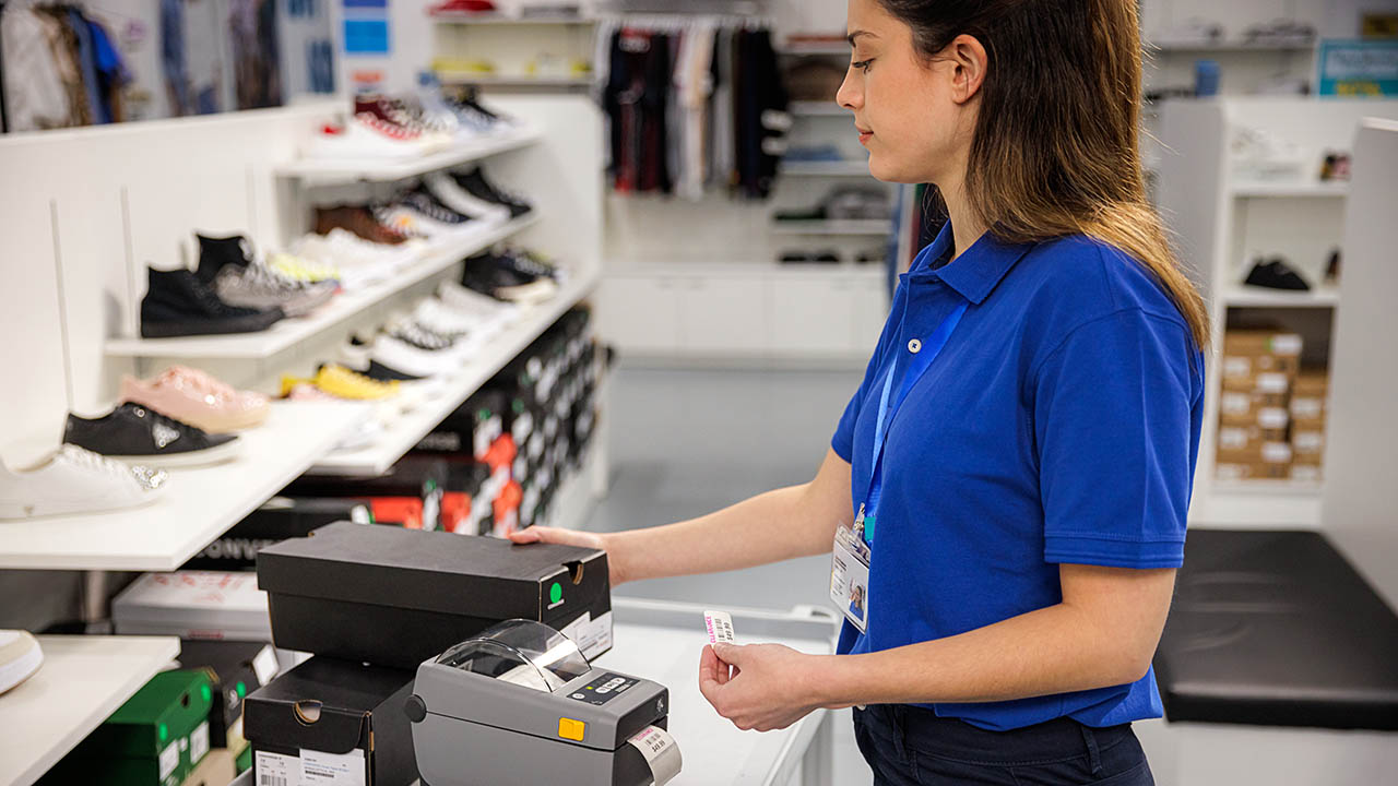 A retail associate prints a price tag for a pair of shoes using a Zebra desktop printer