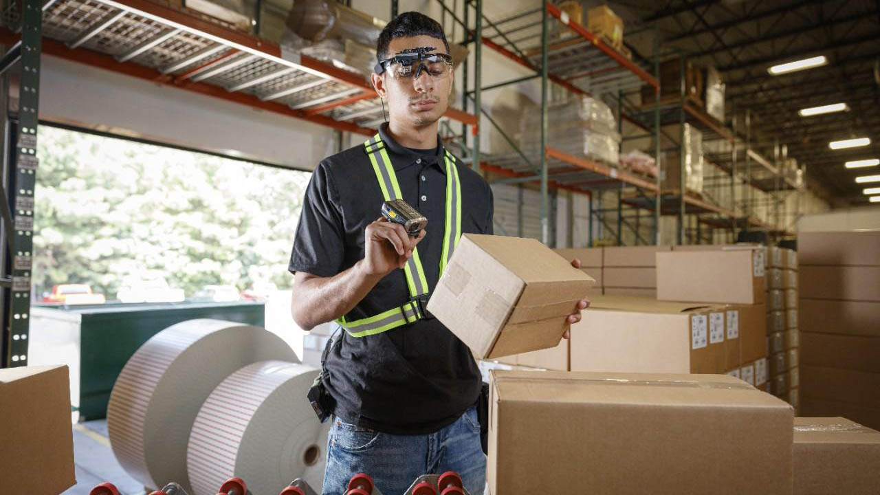 A warehouse worker uses a ring scanner to scan boxes.