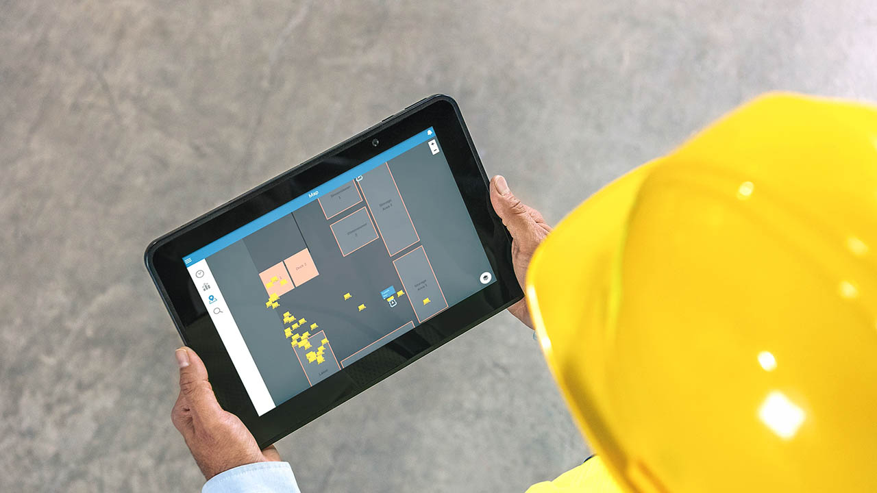 A worker in a hard hat reviews warehouse asset and work movemetns on a Zebra tablet 