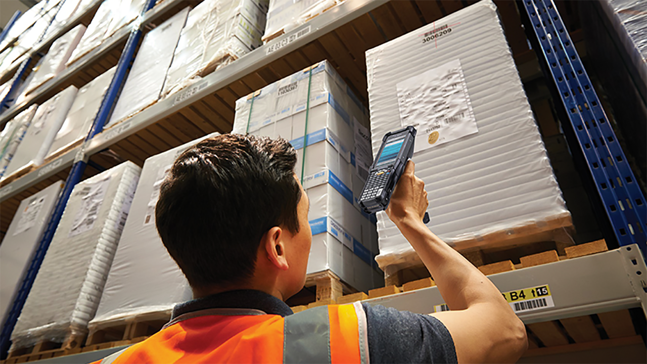 A warehouse worker uses a Zebra long-range mobile computer to scan the barcode on items on a high shelf