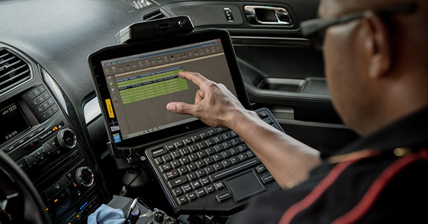Law enforcement using vehicle-mounted touch screen 12.5-inch rugged tablet with full-sized keyboard to retrieve data.