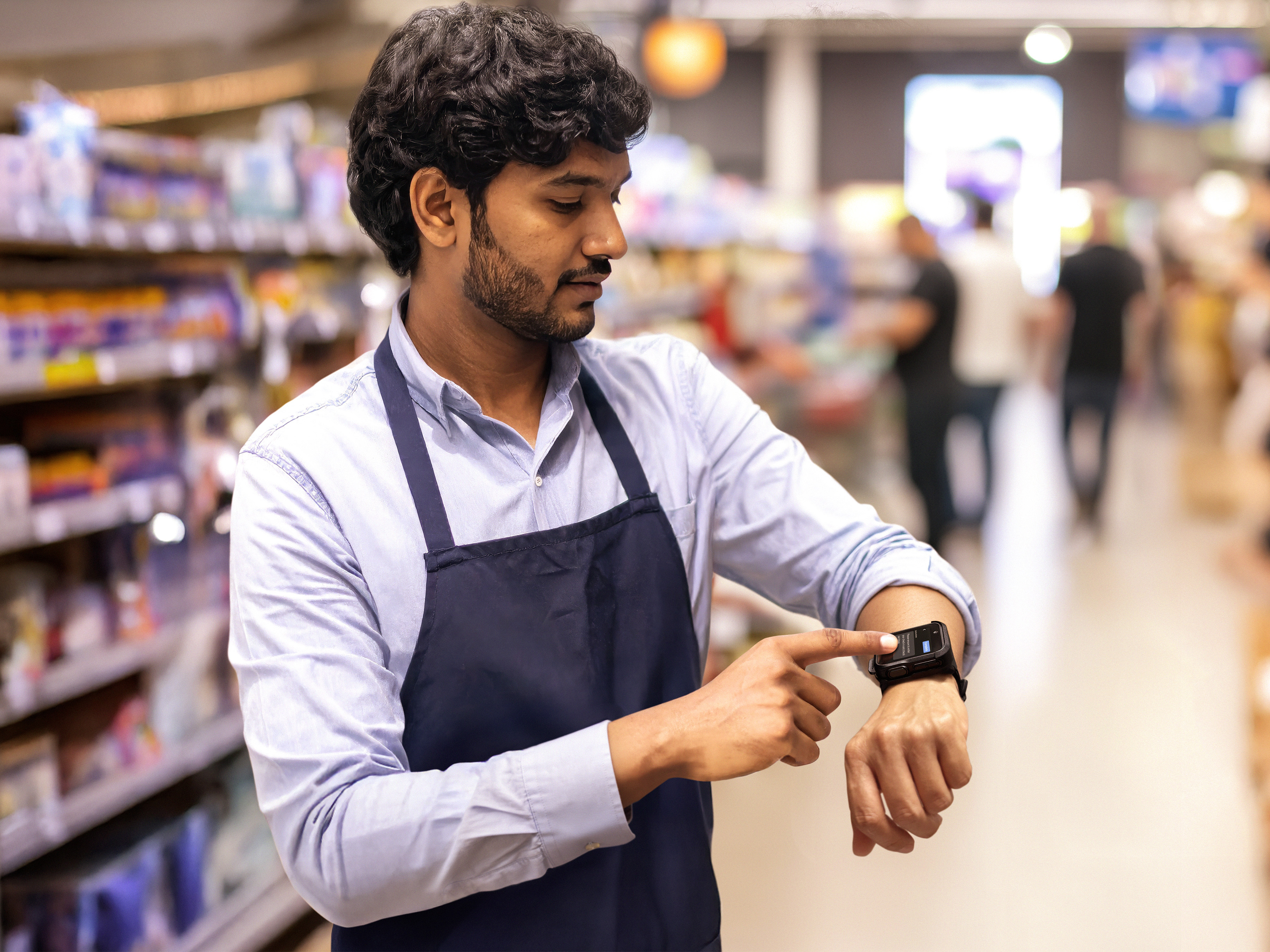 Photo of a retail worker at a grocery store aisle, completing a task with a WS301 on the wrist. This image was generated with the assistance of AI tools and may not depict real people, places, or events.