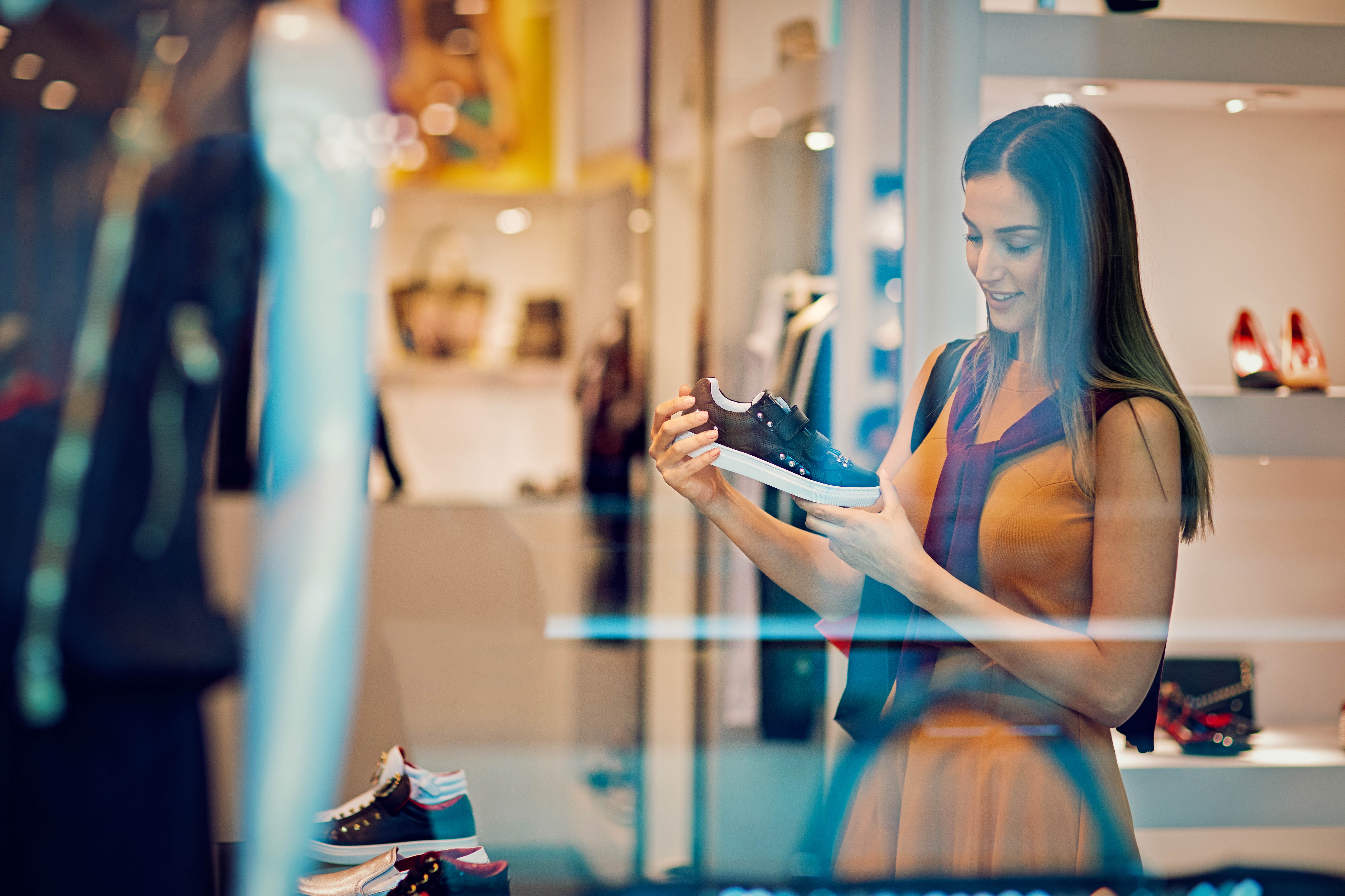 A shopper is looking at a black sneaker with white soles and decorative studs in a retail shoe store.