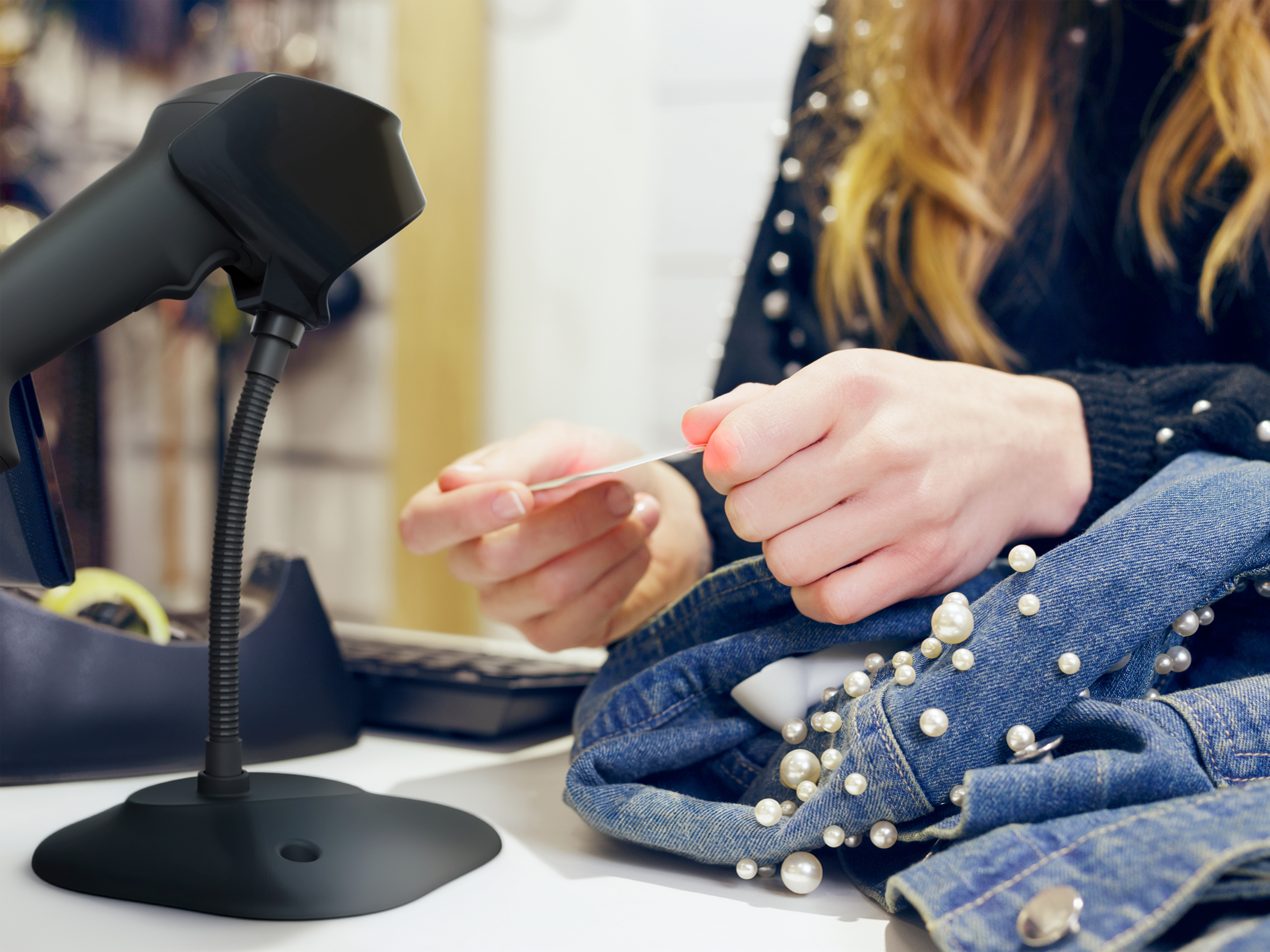 Close-in shot of a retail employee using a scanner in a gooseneck stand to scan a tag on a jacket.