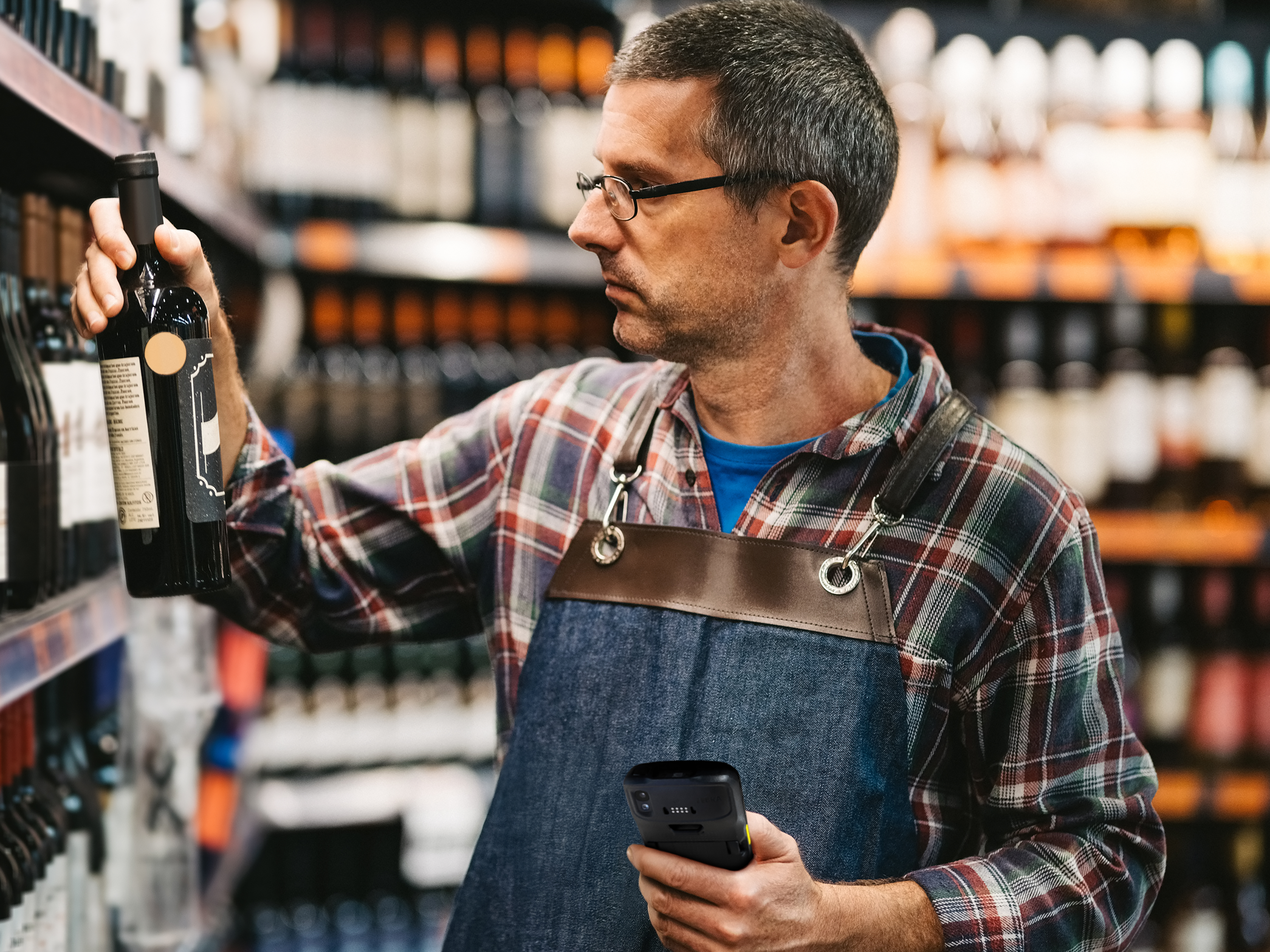 Retail employee scans a wine bottle in store aisle, checking product details while organizing inventory