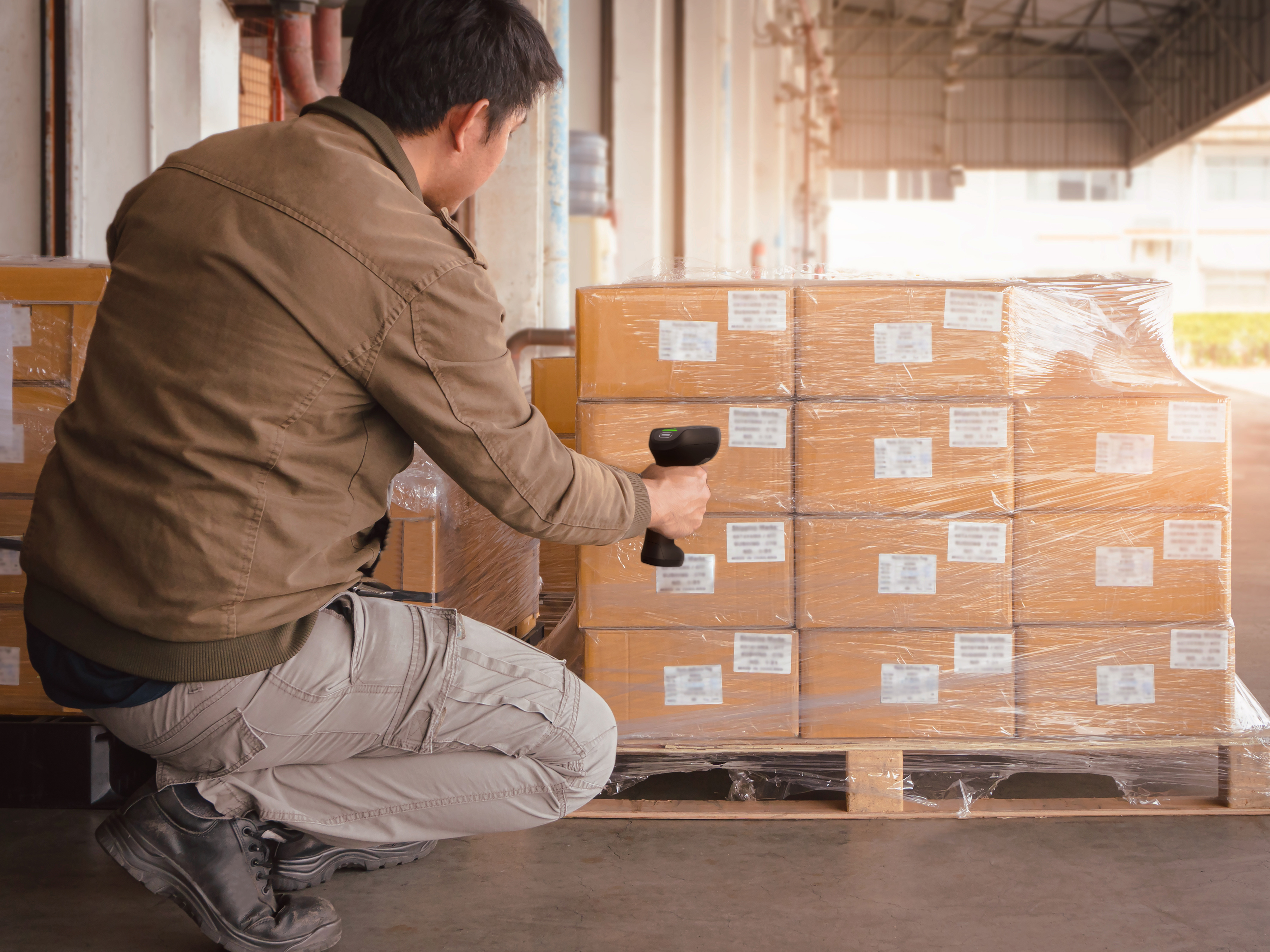 Warehouse employee uses a handheld scanner to scan the barcodes of boxes on a pallet.