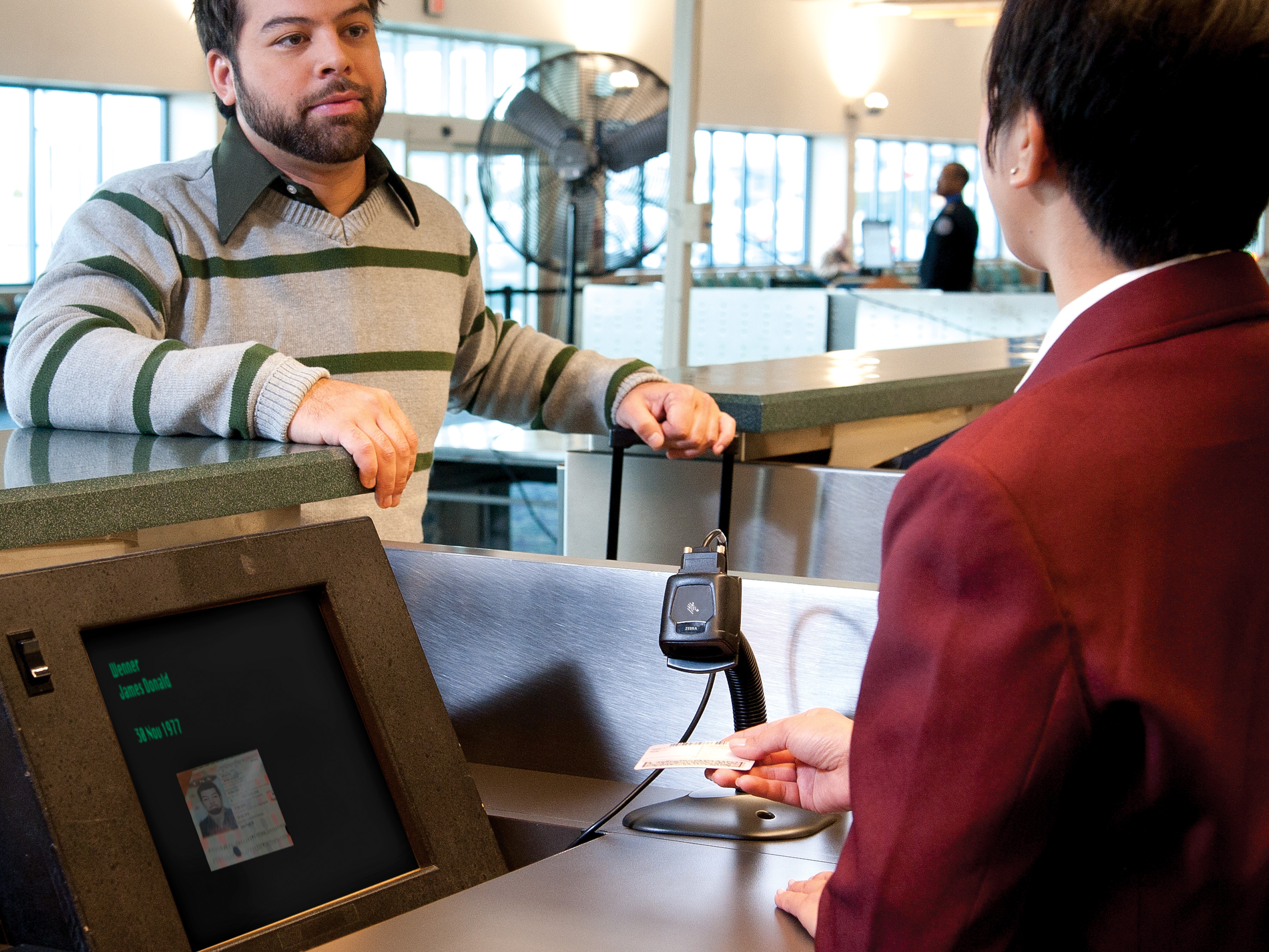 Worker uses Zebra barcode scanner on a fixed mount to scan a driver's license