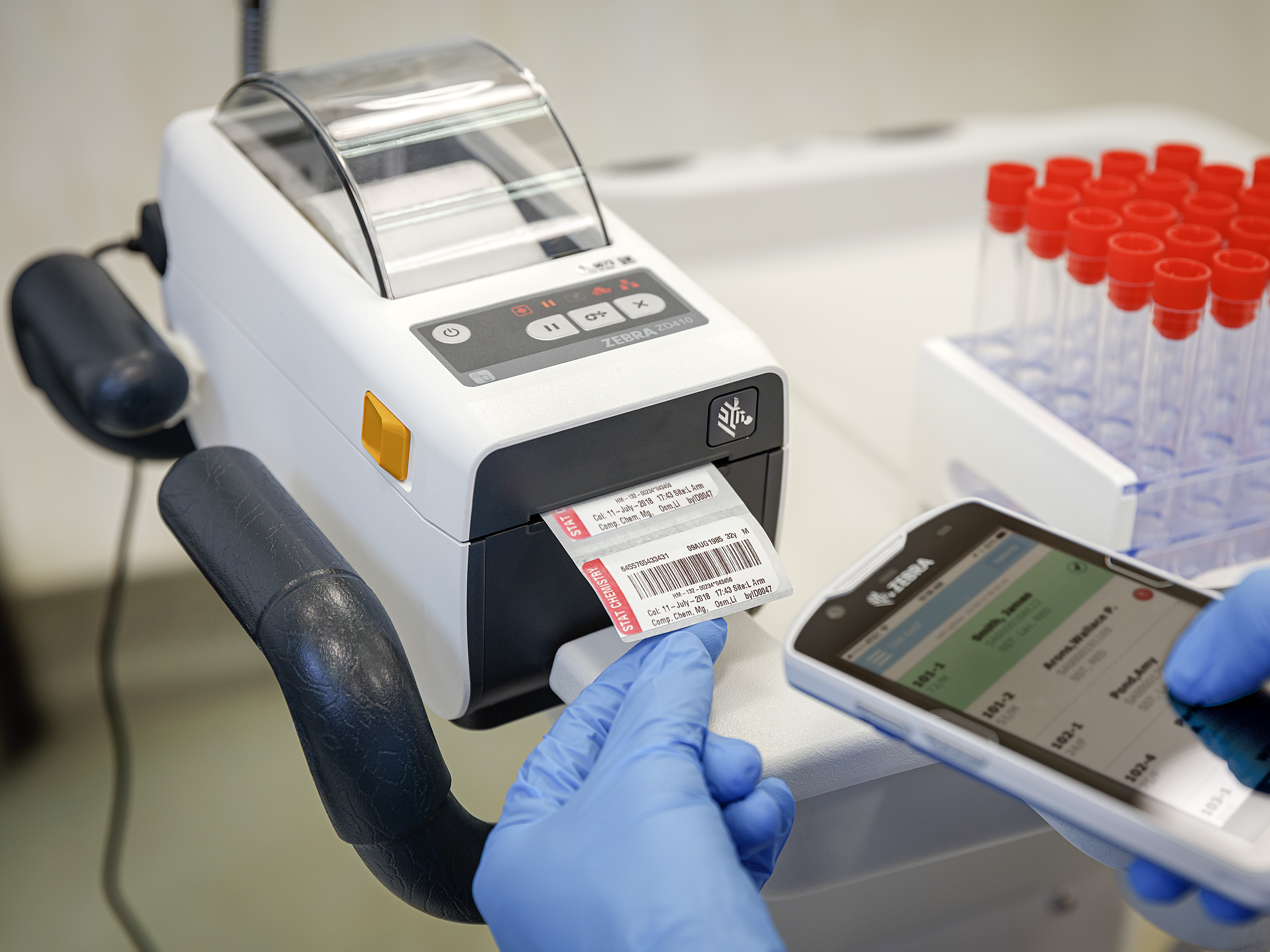 A healthcare worker uses a Zebra mobile computer to scan a label coming out of a Zebra printer.