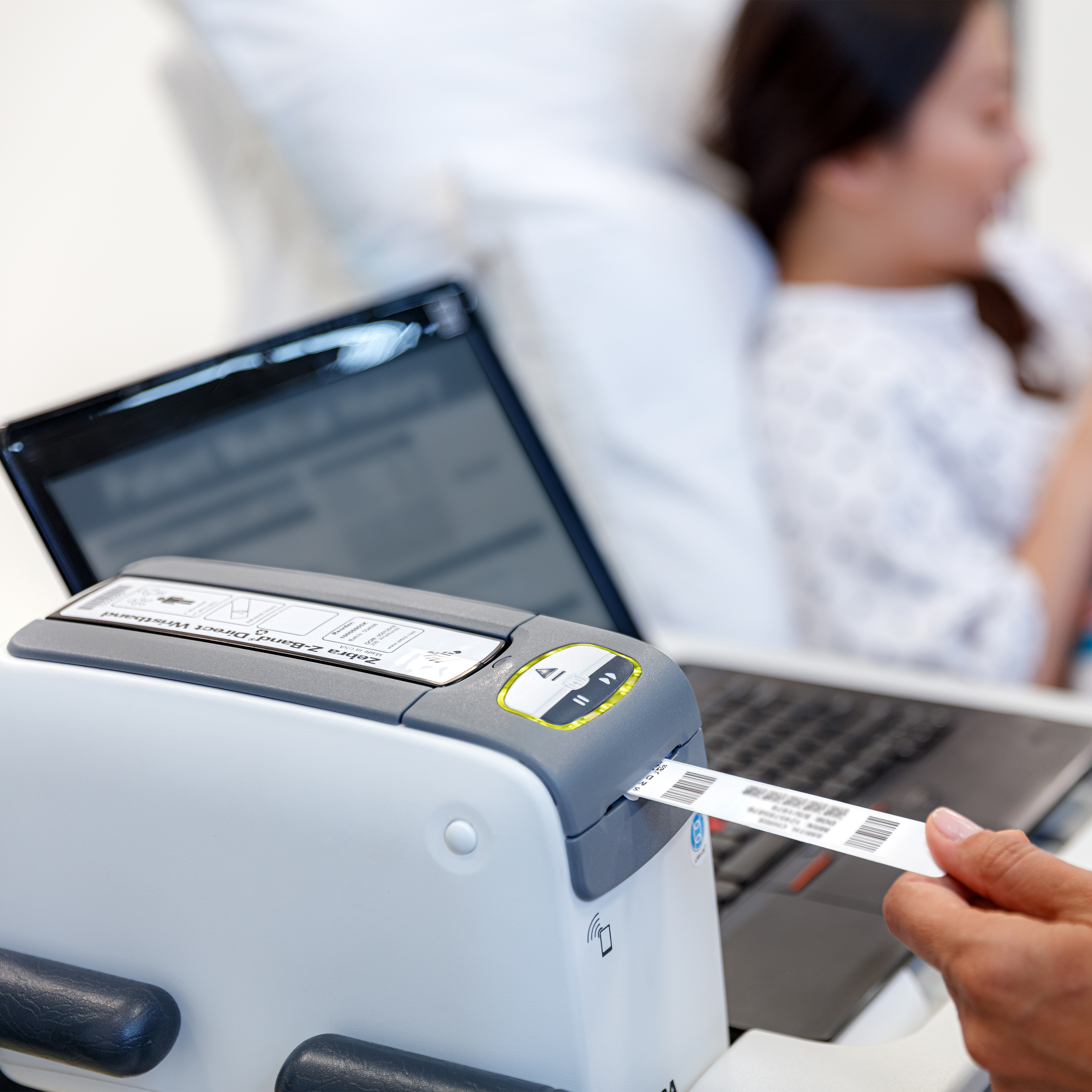 A clinician in a hospital uses a white Zebra ZD510-HC wristband printer to print a barcode wristband at the patient's bedside.
