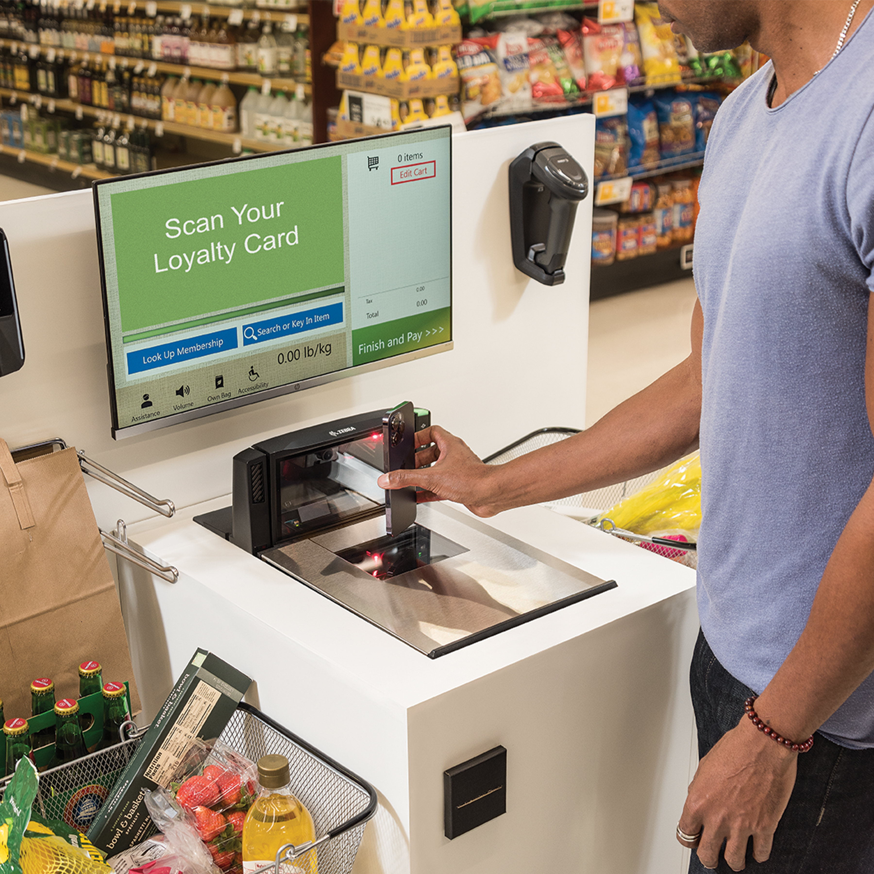 A customer scans a digital loyalty card from their mobile phone using Zebra’s MP72 bioptic scanner at a grocery self-checkout lane. This next-generation upgrade balances aggressive scan speeds and superior mobile screen readability with frictionless automated IT deployment using 123Scan software, minimizing checkout friction and retail operational downtime.
