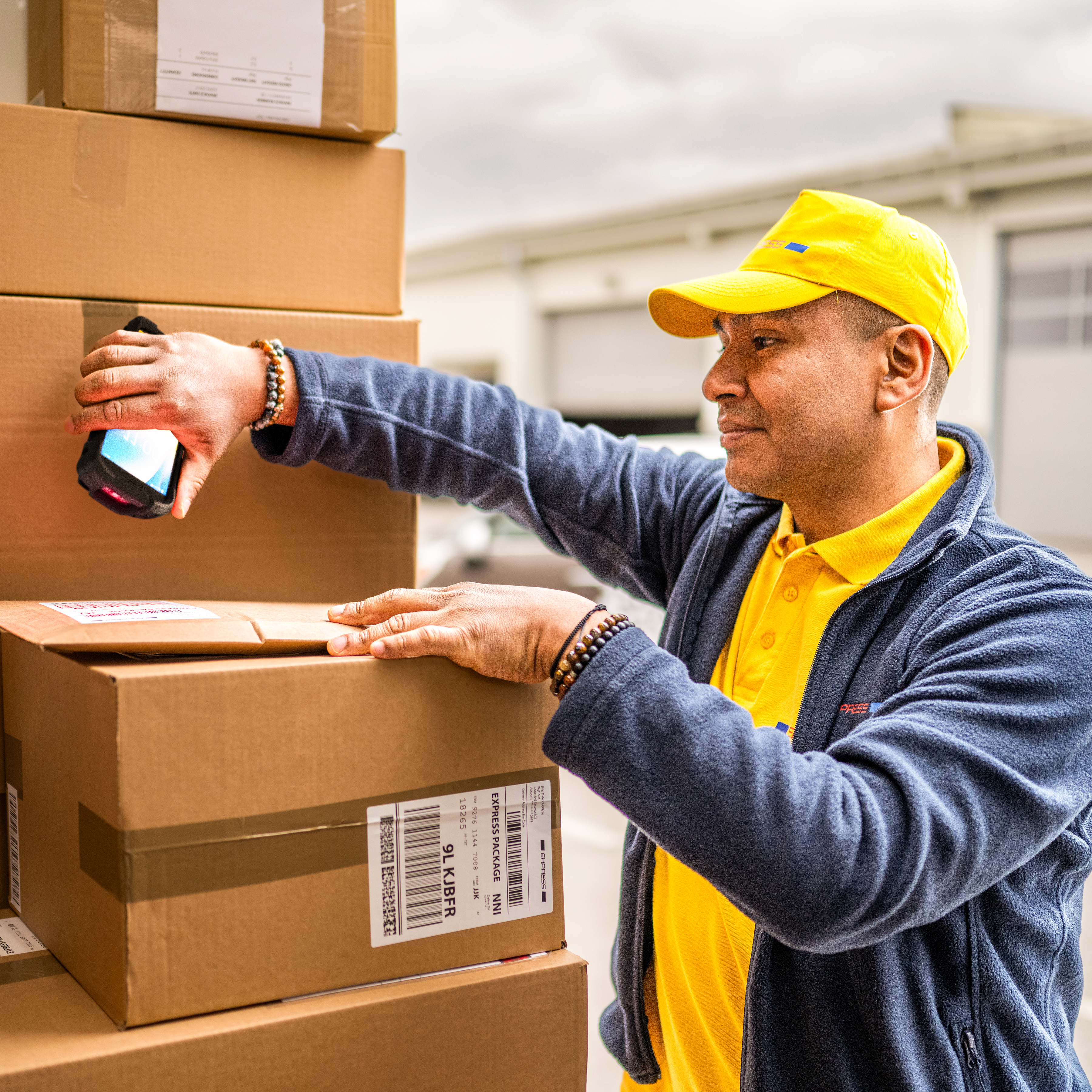 A transportation and logistics worker using a handheld mobile computer to scan packages inside the back of a delivery truck.