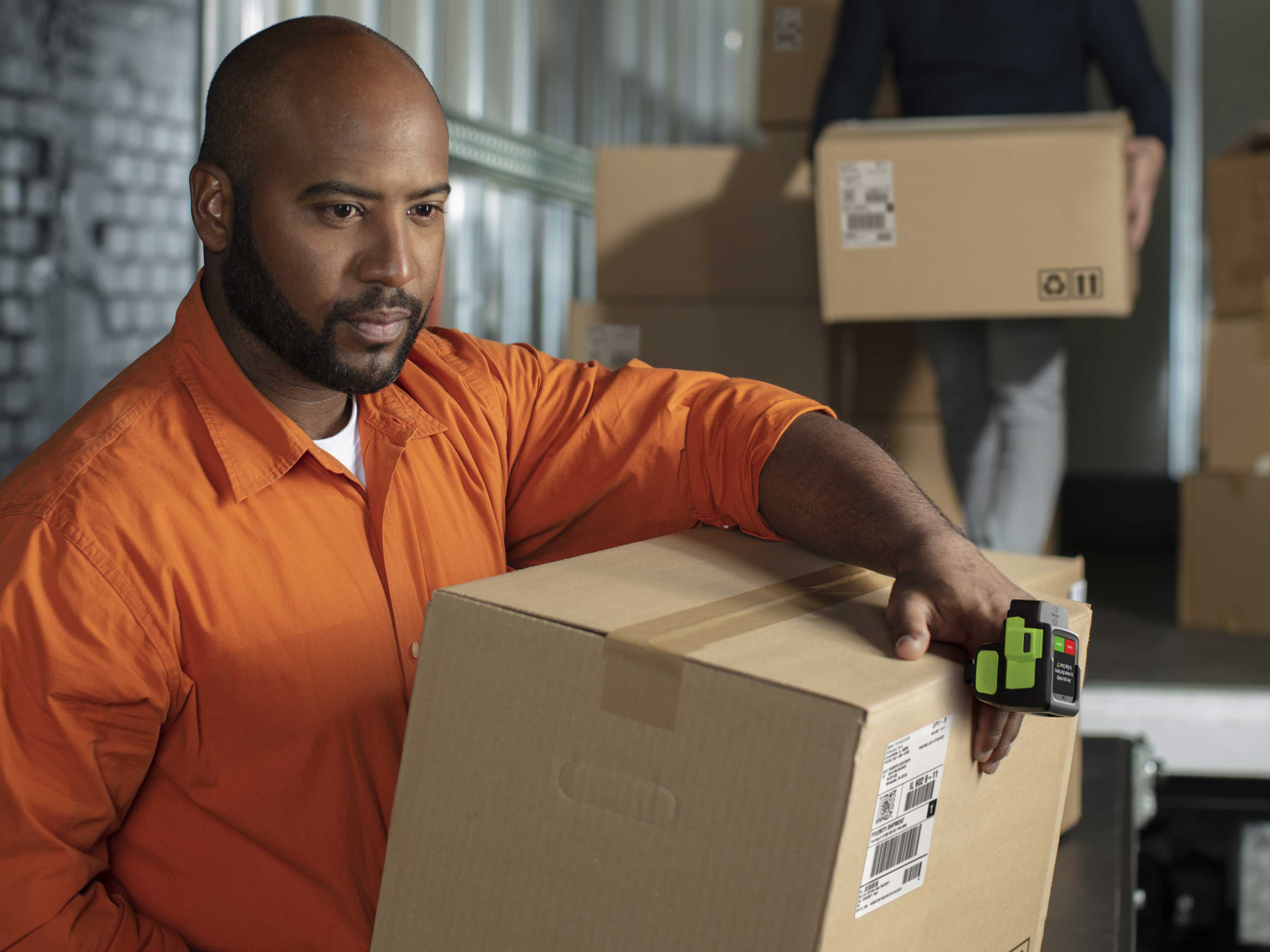 A warehouse worker uses a Zebra WS50 finger-mounted mobile computer to scan a package while unloading boxes from a truck.