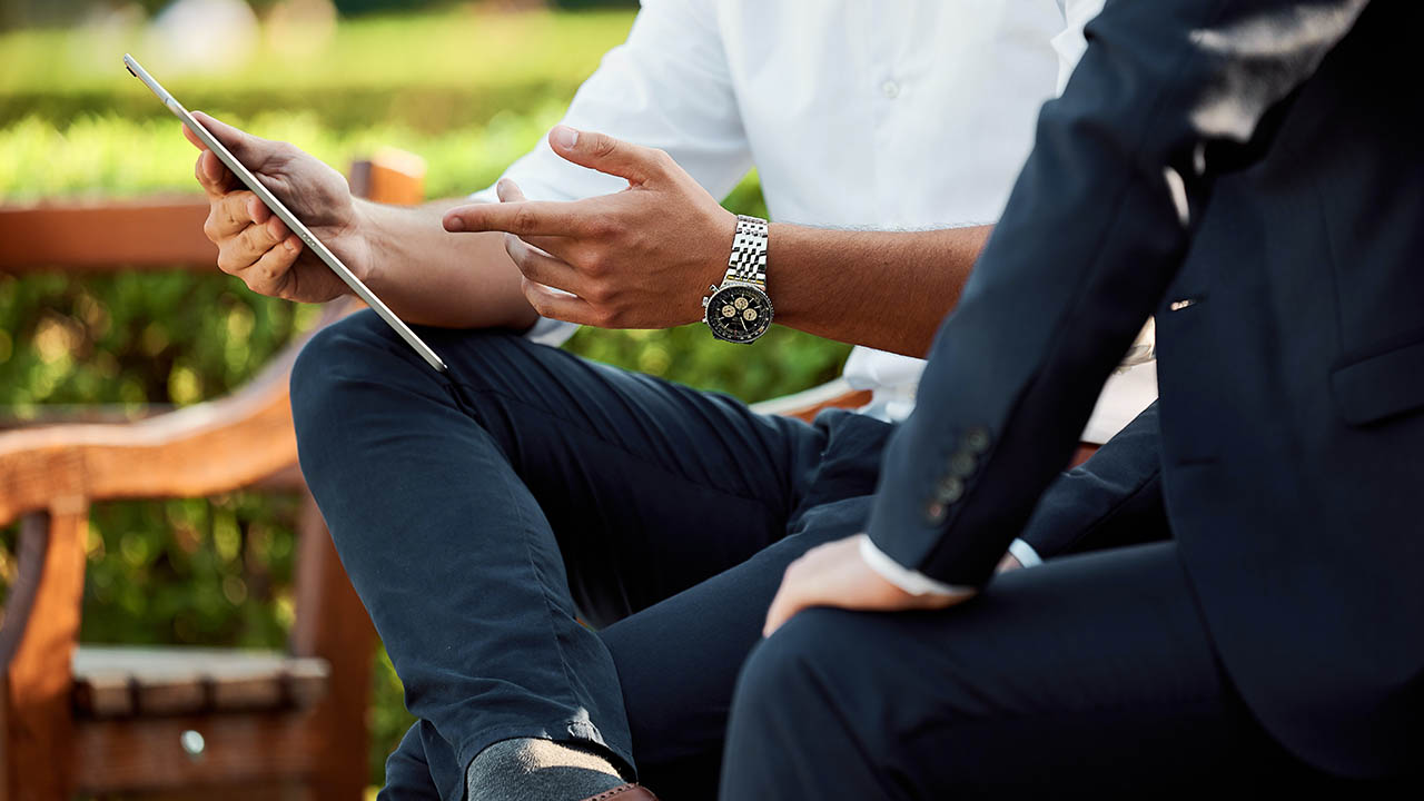 Two people sit on a bench looking at a tablet