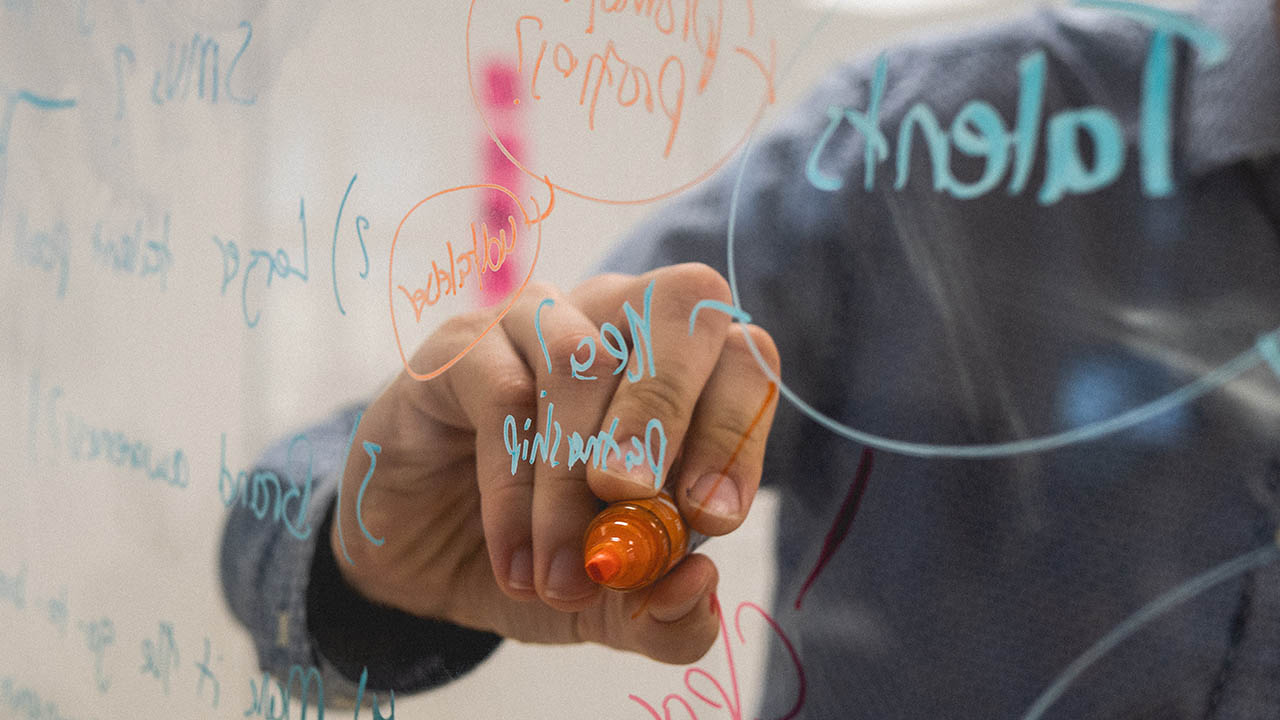 A person writing on a clear dry erase board