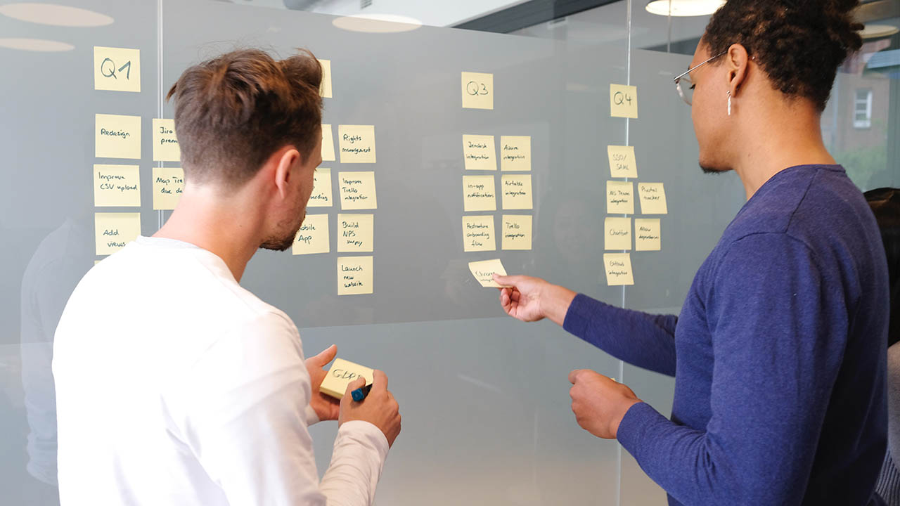 Two men stand at a brainstorm board full of sticky notes