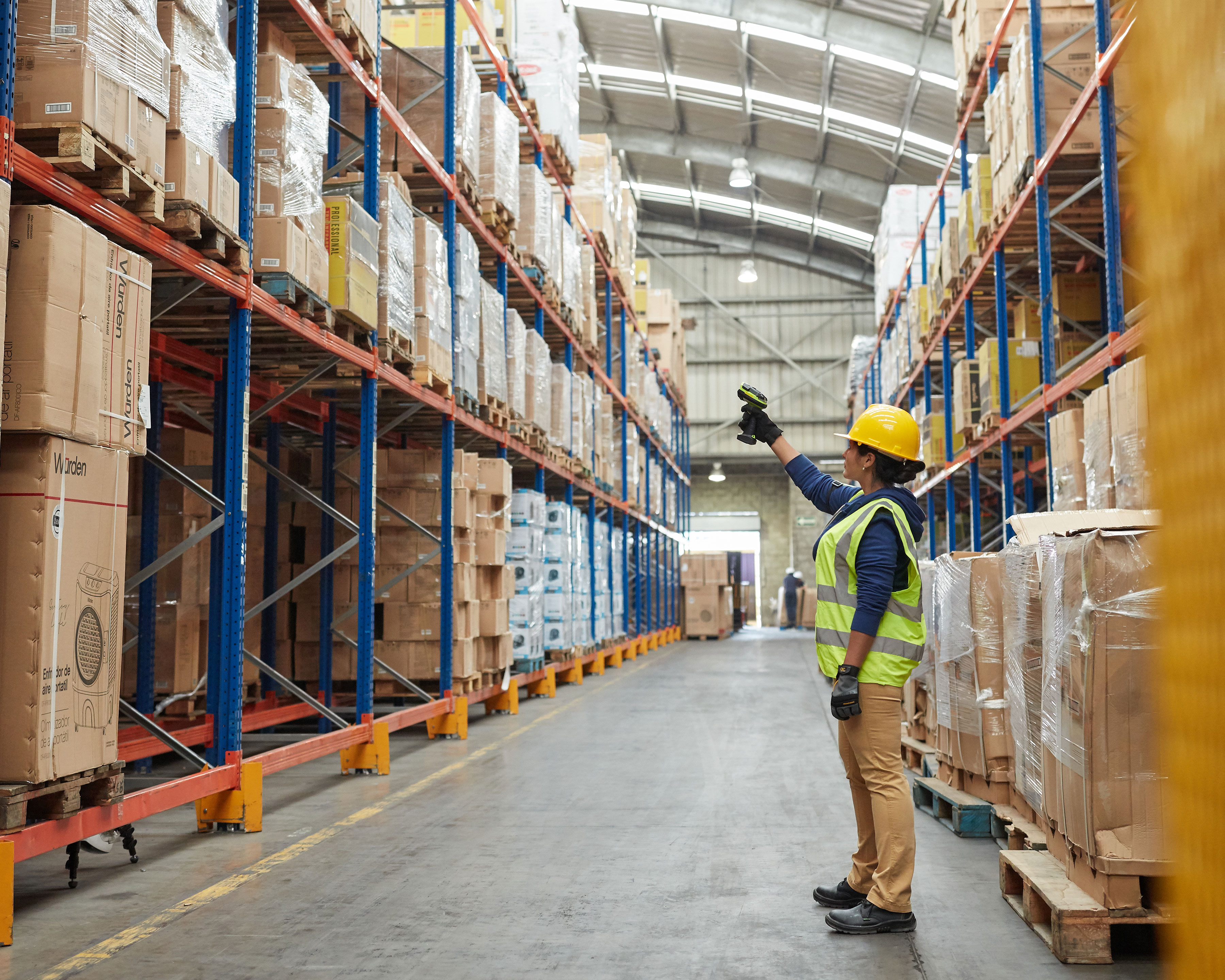 Warehouse worker uses Zebra DS3600 long range barcode scanner to scan brown boxes on top of pallet racks 