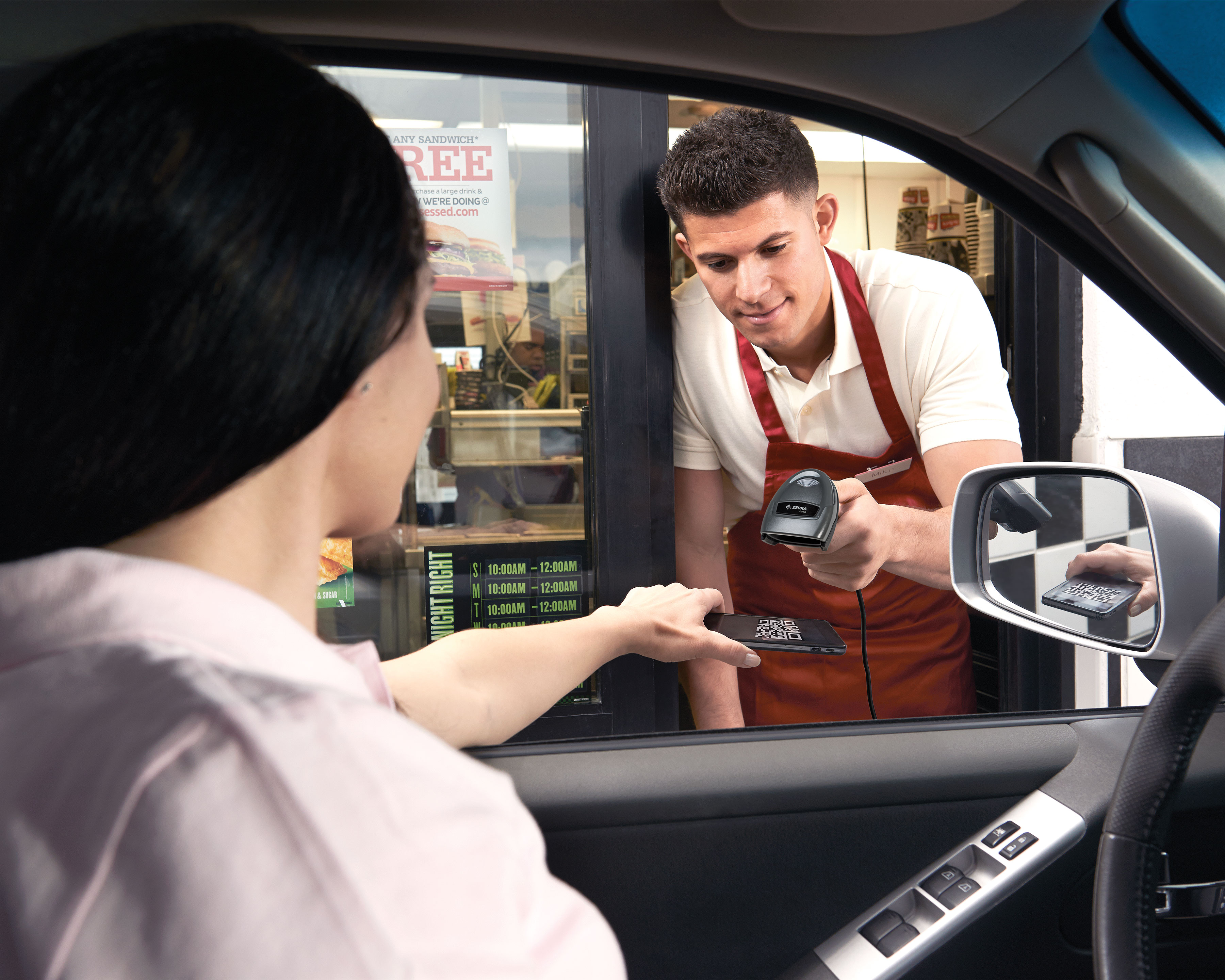 Fast food worker uses the Zebra DS4600 retail handheld scanner to scan a QR code displayed on a customer's mobile phone in a drive through