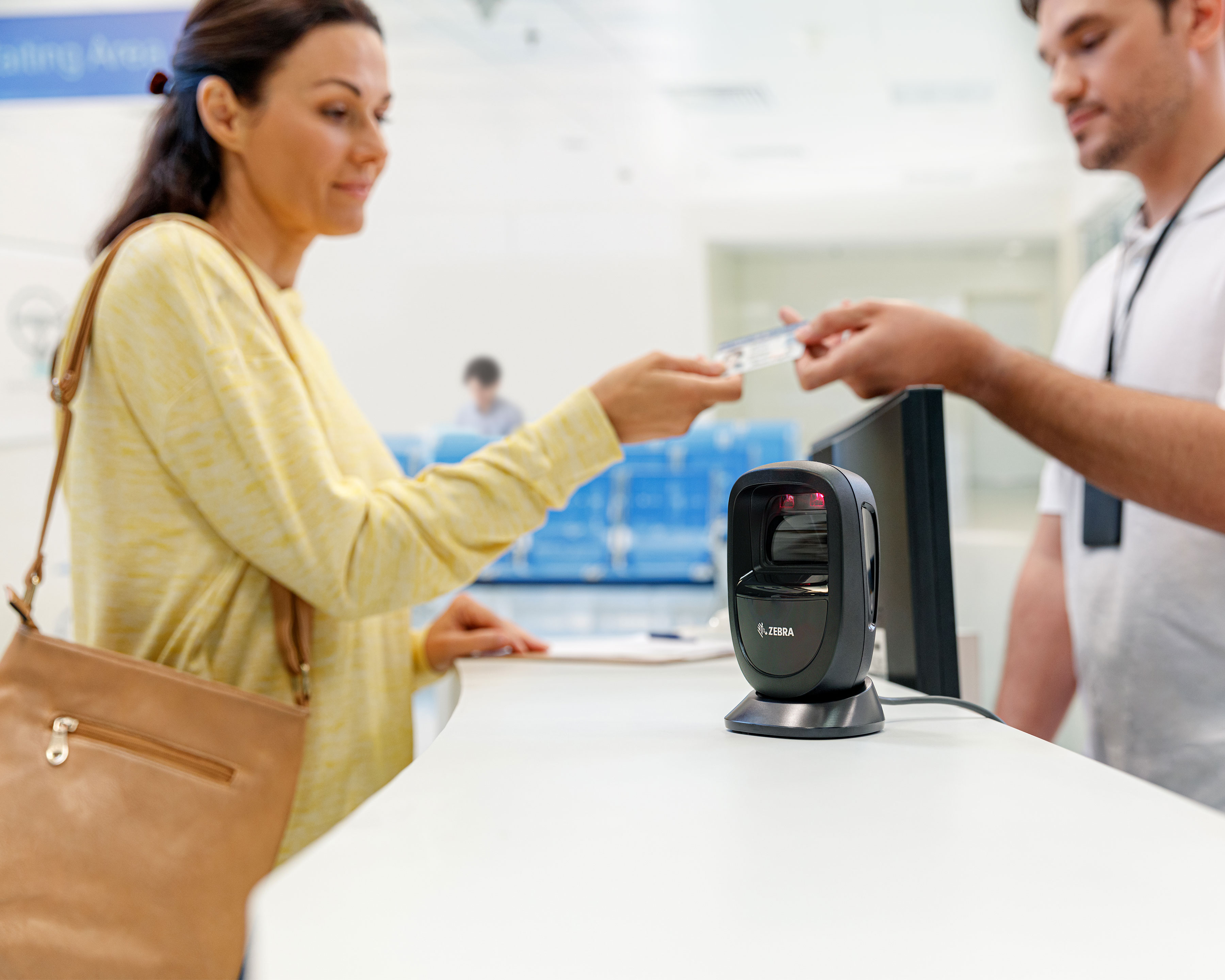 Zebra DS9300 hands free barcode scanner sits on counter as woman hands her driver's license to a DMV employee