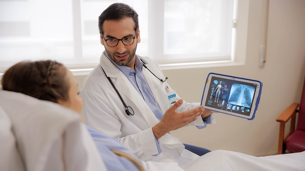 A doctor reviews radiology imaging with a patient at the bedside using a Zebra ET4x-HC healthcare-grade tablet