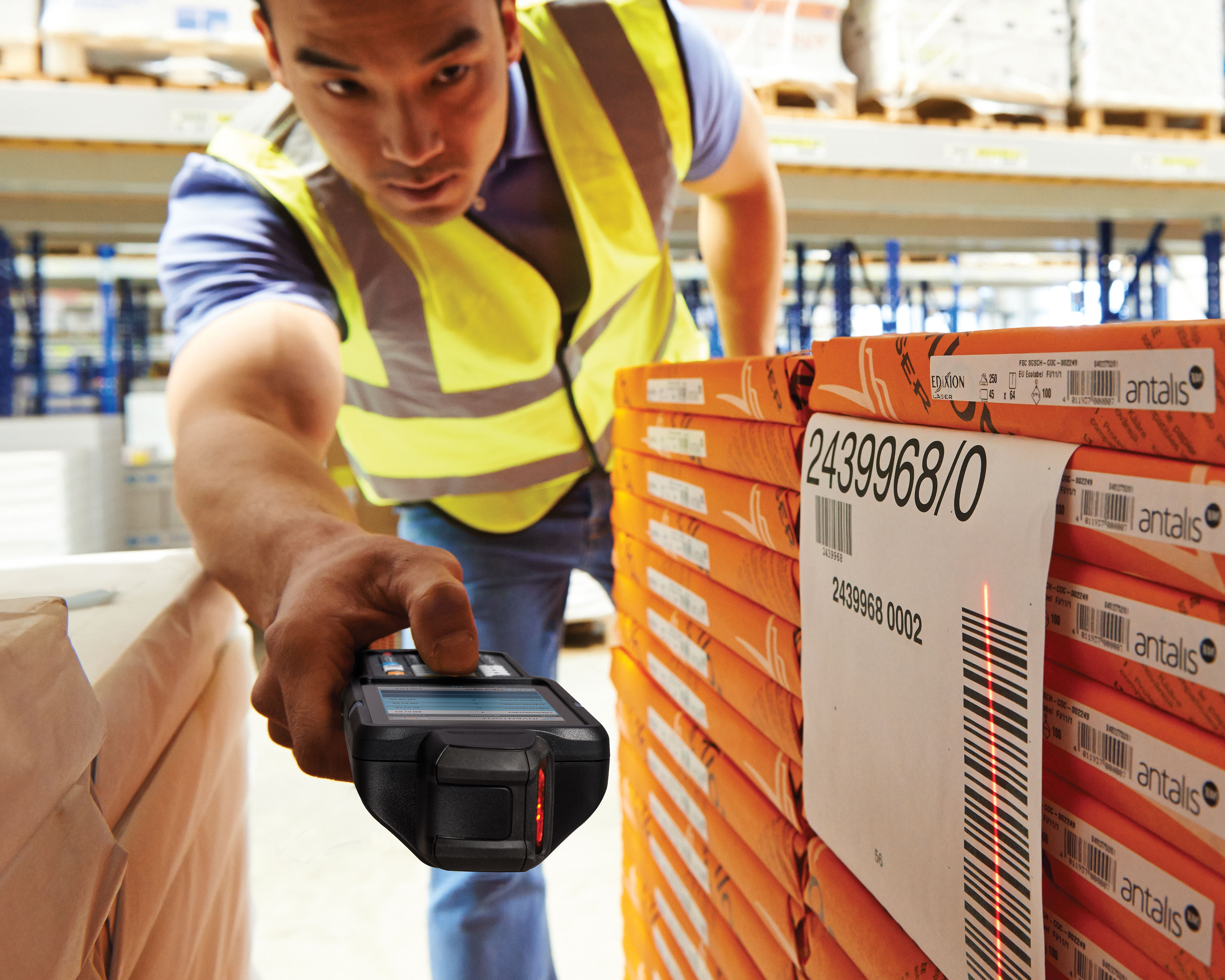 Warehouse worker uses Zebra MC3300 mobile computer with a rotating turret to scan a barcode label in a tight space between two stacks of inventory