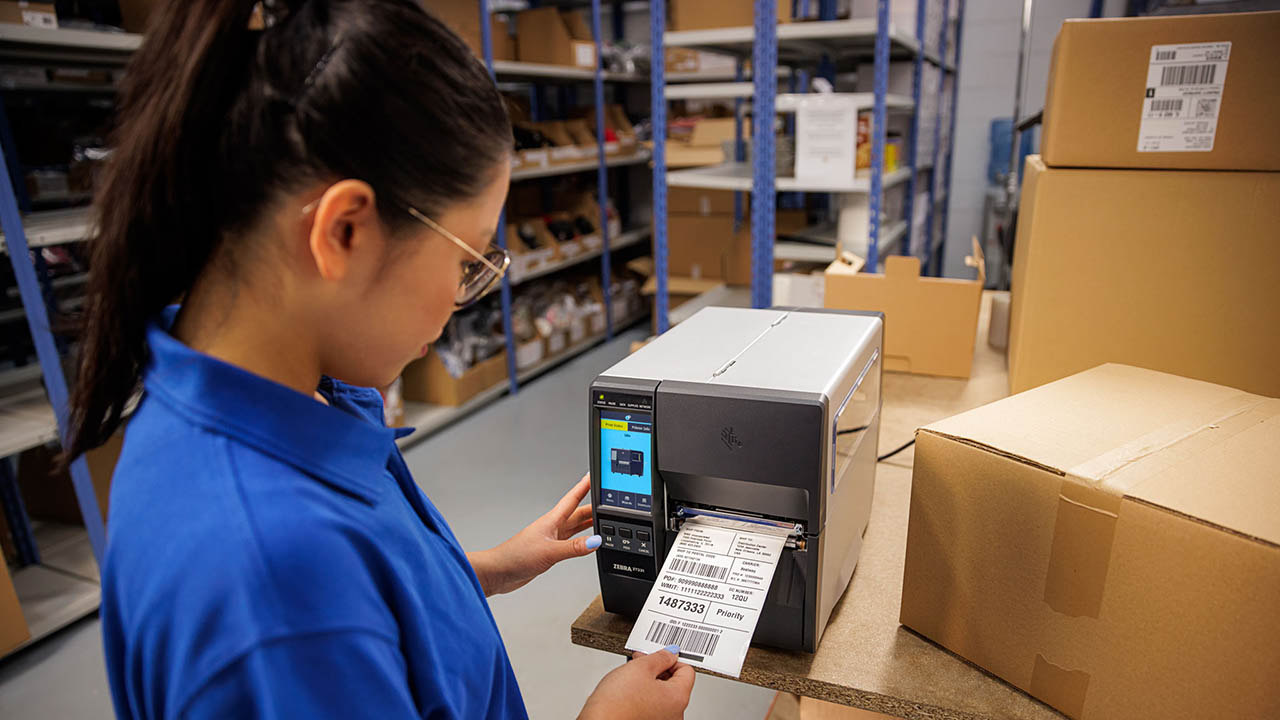 A retail associate pulls a shipping label off a Zebra ZT231 industrial printer