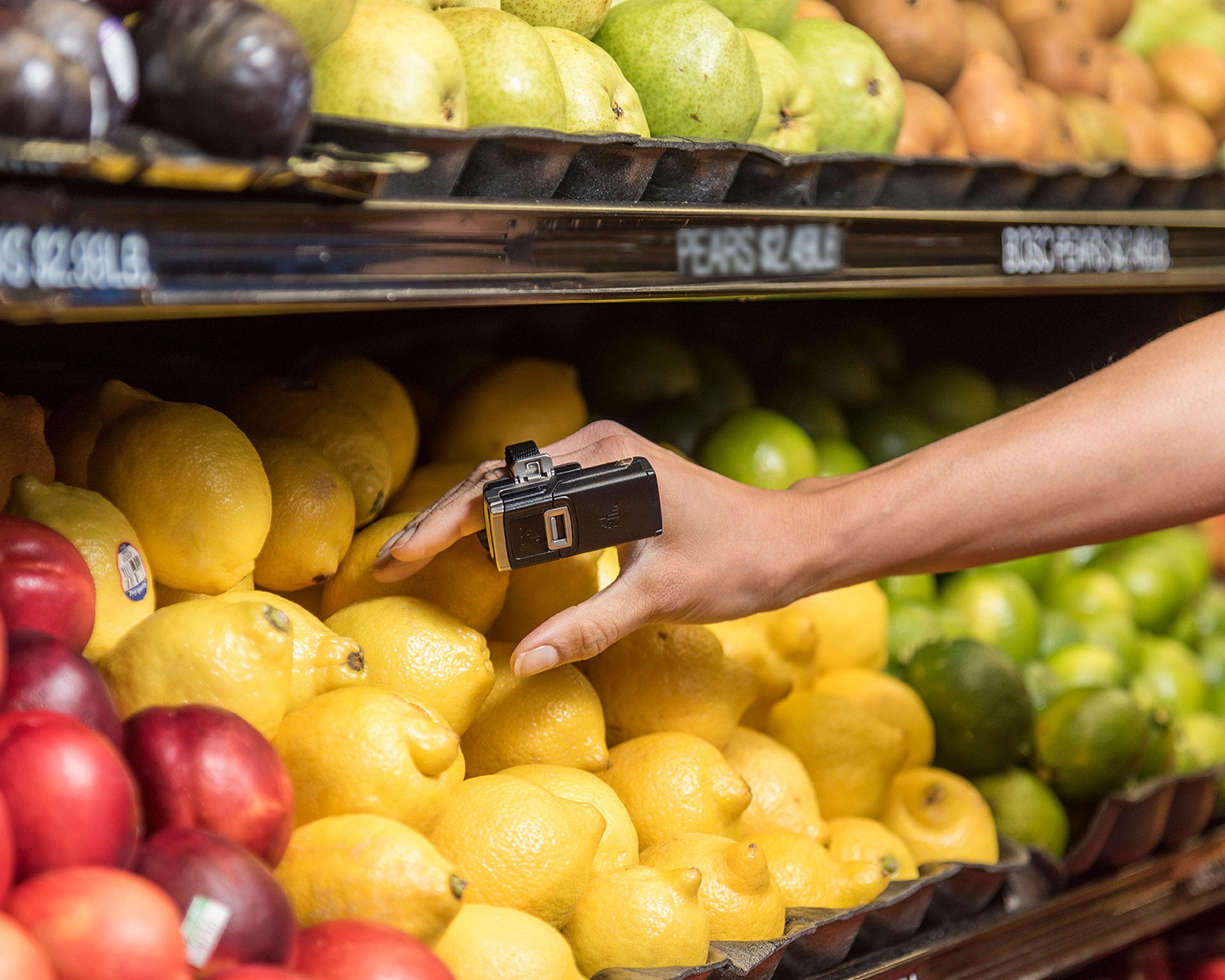 Grocery store worker wears Zebra RS5100 wireless Bluetooth barcode scanner on her index finger as she collects a lemon