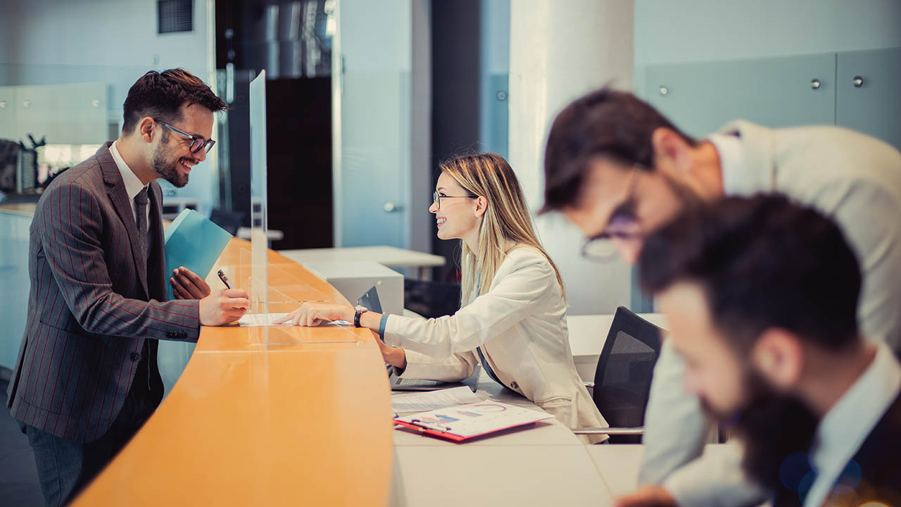 A young man is standing at a bank counter. Because of the good negotiation skills of an efficient employee, he decided to cooperate with her and sign a contract.