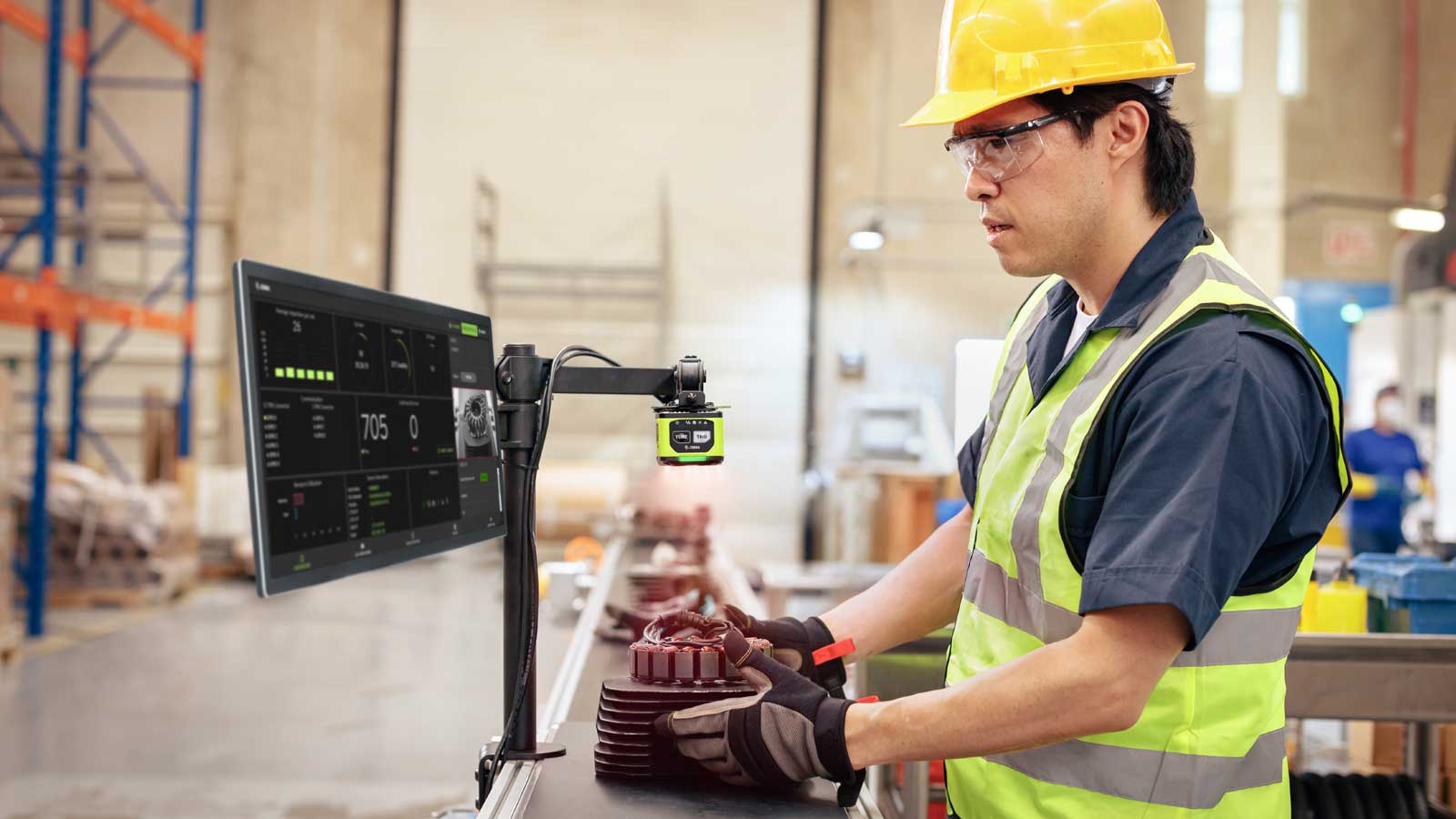 A manufacturing worker performs a quality check on a part using a Zebra FS40 Fixed Industrial Scanner and VS40 Smart Camera, with real-time analytics displayed on a monitor.
