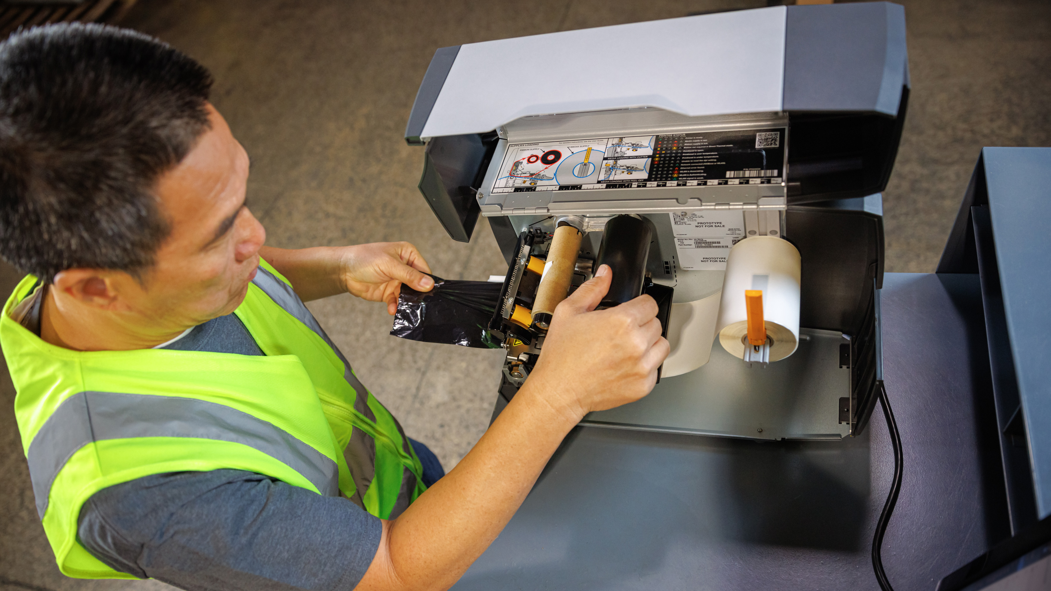 A worker loading a new label roll in a Zebra thermal printer.
