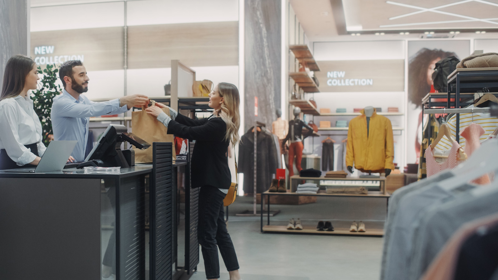 A customer hands a shopping bag to a cashier at a modern clothing store that leverages actionable intelligence and its use of inventory data to optimize sales.