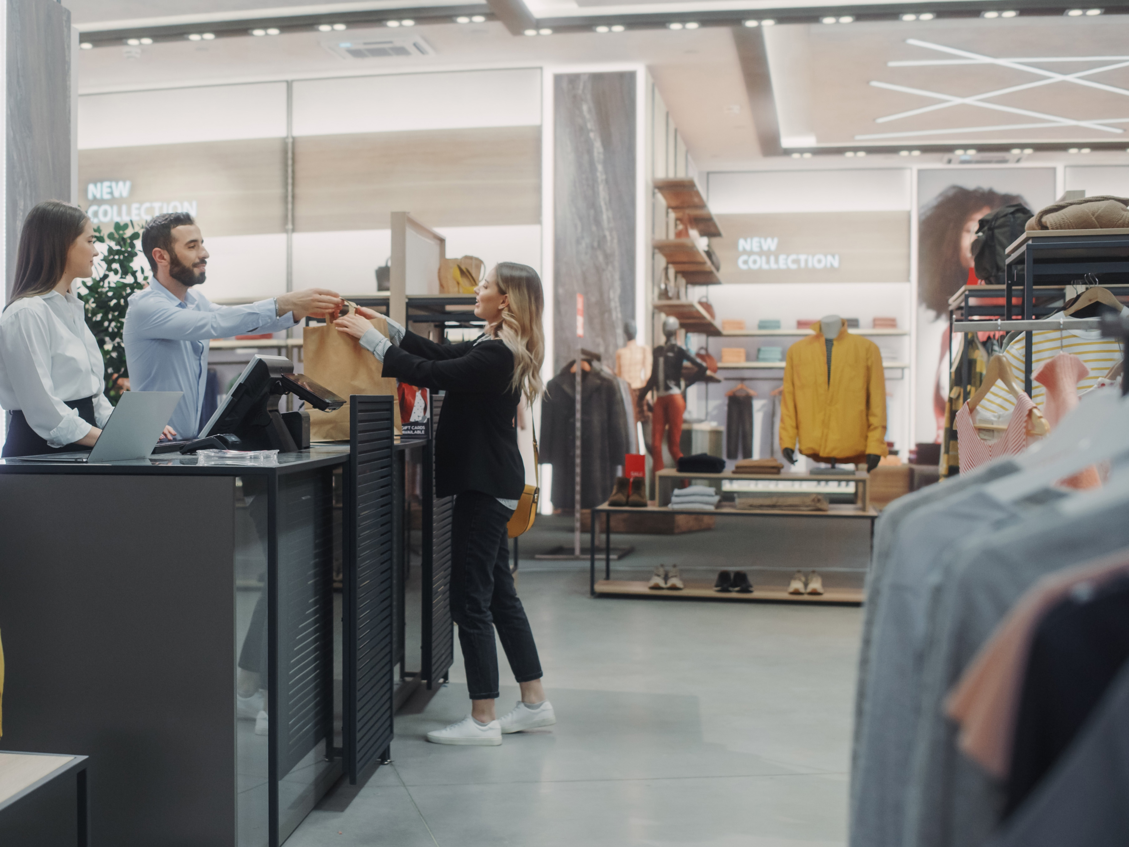 A customer hands a shopping bag to a cashier at a modern clothing store that leverages actionable intelligence and its use of inventory data to optimize sales.