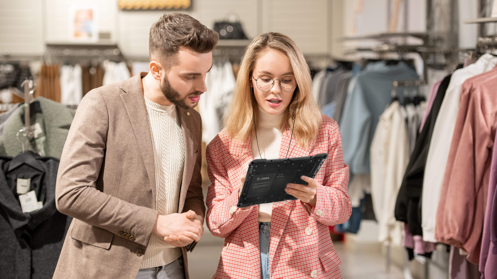 A retail associate uses a Zebra rugged tablet to instantly meet customer demand by assisting a shopper in a modern clothing store.