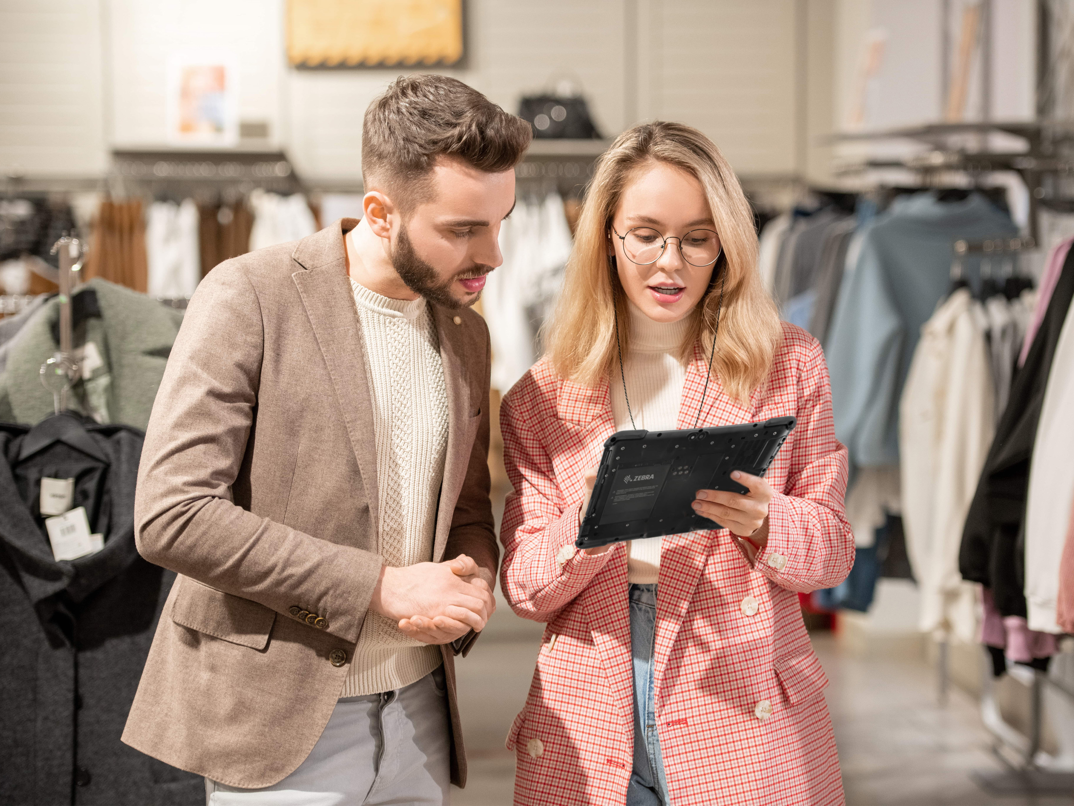 A retail associate uses a Zebra rugged tablet to instantly meet customer demand by assisting a shopper in a modern clothing store.