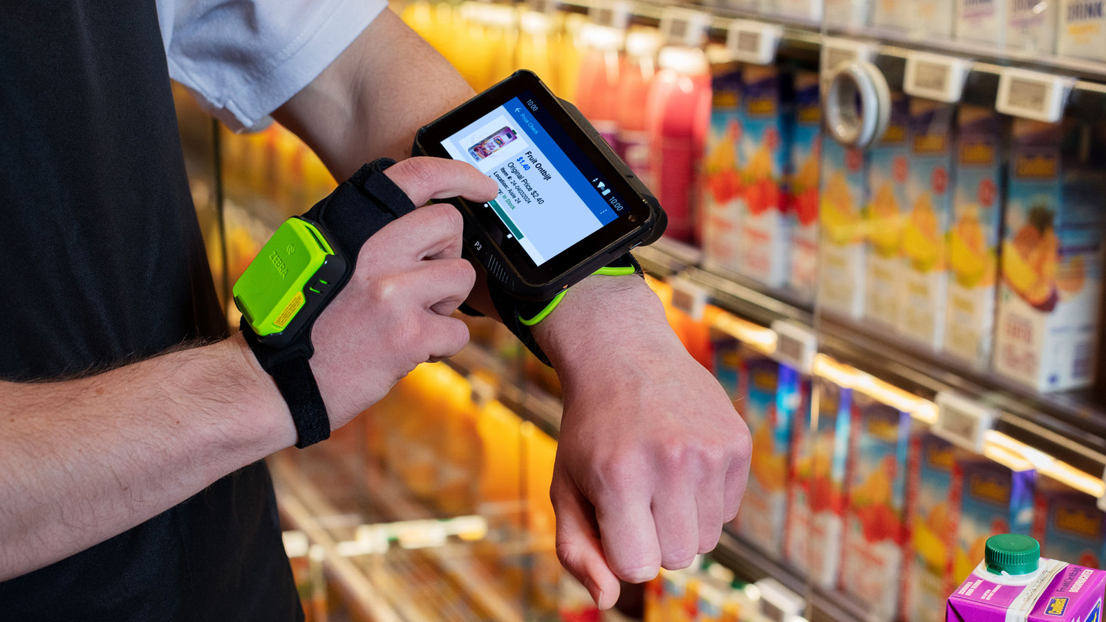 A worker in a grocery isle is using a Zebra mobile computer and ring scanner to perform a price check for fruit drinks.