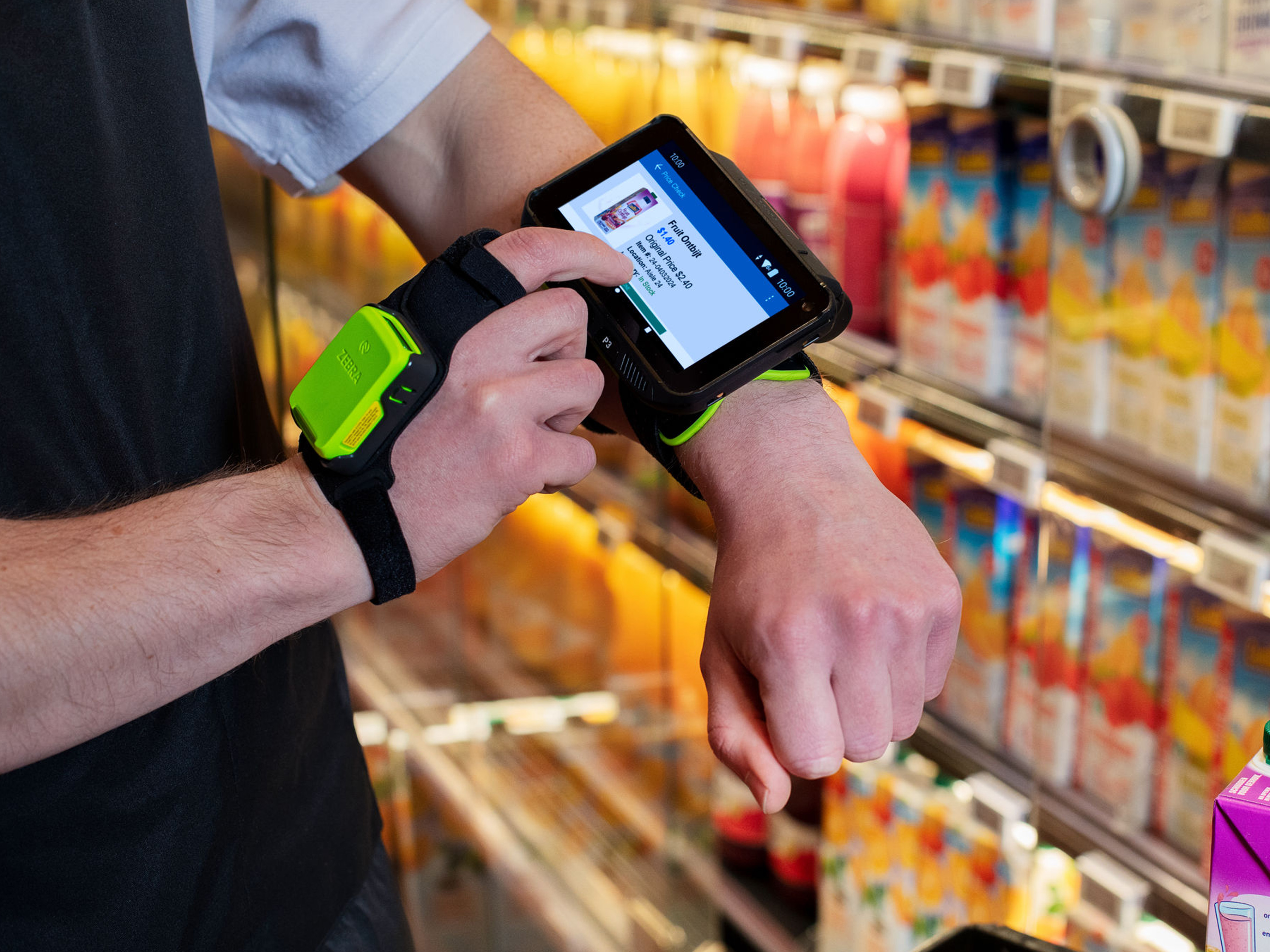 A worker in a grocery isle is using a Zebra mobile computer and ring scanner to perform a price check for fruit drinks