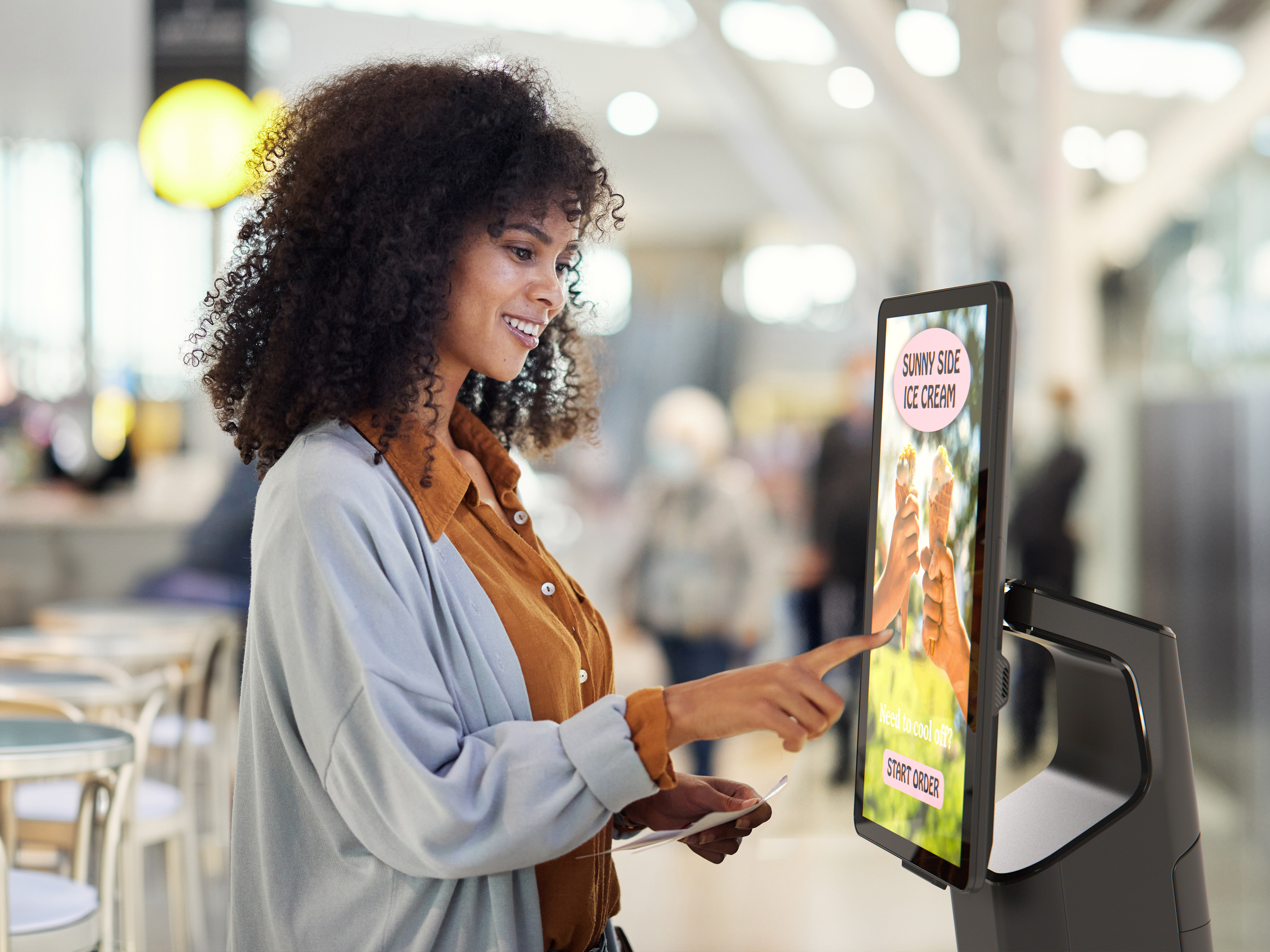 A woman is using a Zebra application kiosk system for self-service ordering in a restaurant to buy ice cream.