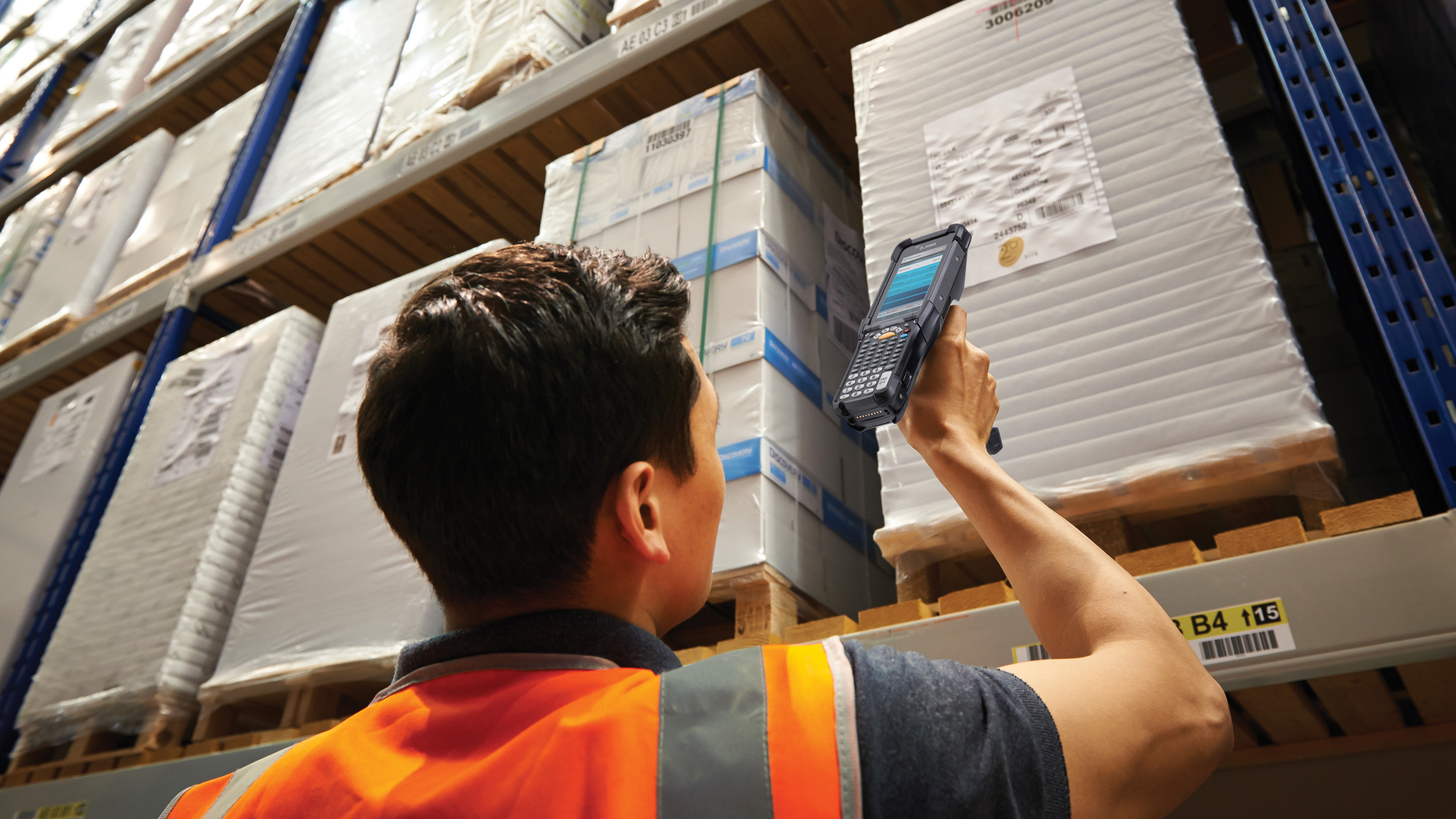 From a far distance, a warehouse employee scans a barcode on a pallet positioned at a great height using a Zebra mobile touch computer.