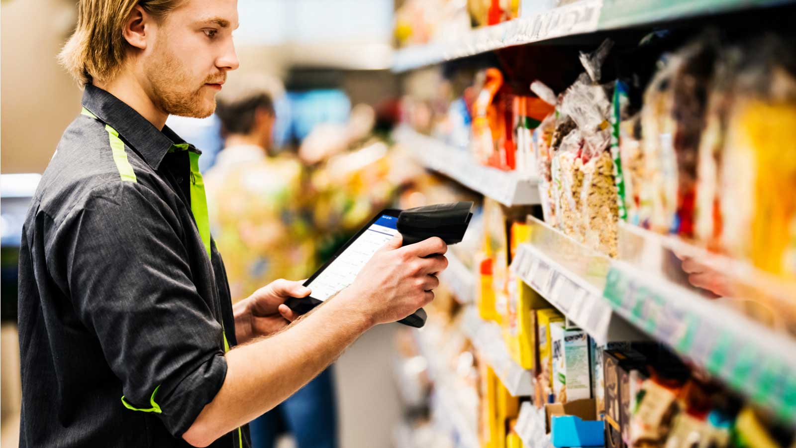 A retail associate uses a Zebra handheld mobile computer and barcode scanner to manage inventory and check prices on products in a grocery store aisle.