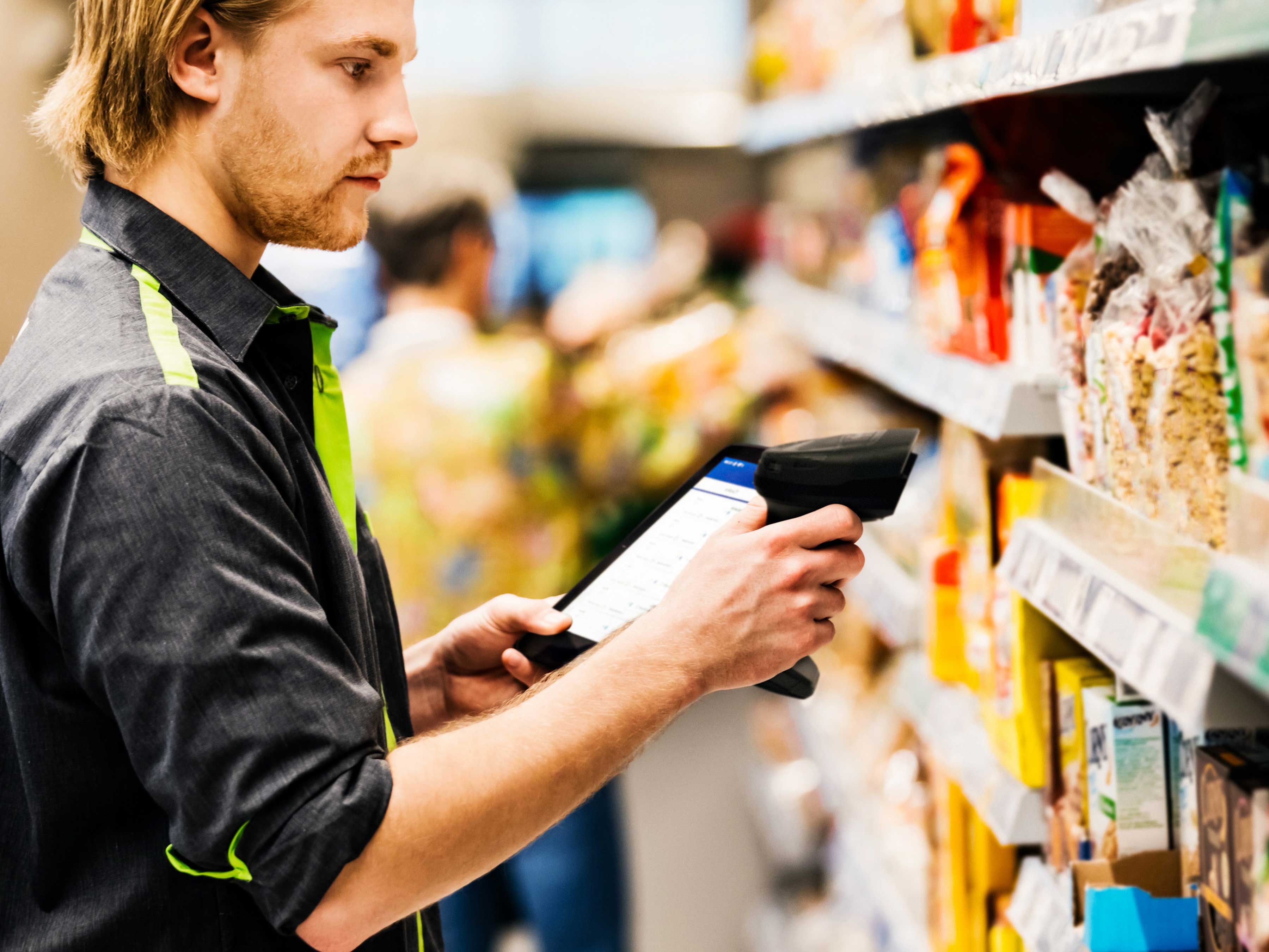 A retail associate uses a Zebra handheld mobile computer and barcode scanner to manage inventory and check prices on products in a grocery store aisle.