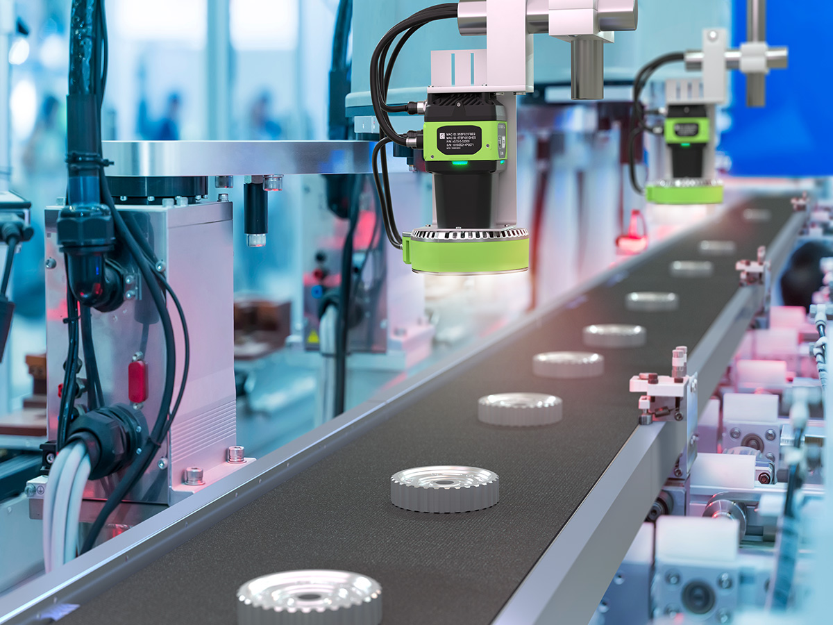 In an industrial manufacturing plant, smart cameras positioned at a conveyor belt inspect metal gears, using advanced algorithms to ensure quality by detecting imperfections in real-time as the gears pass beneath their lenses.
