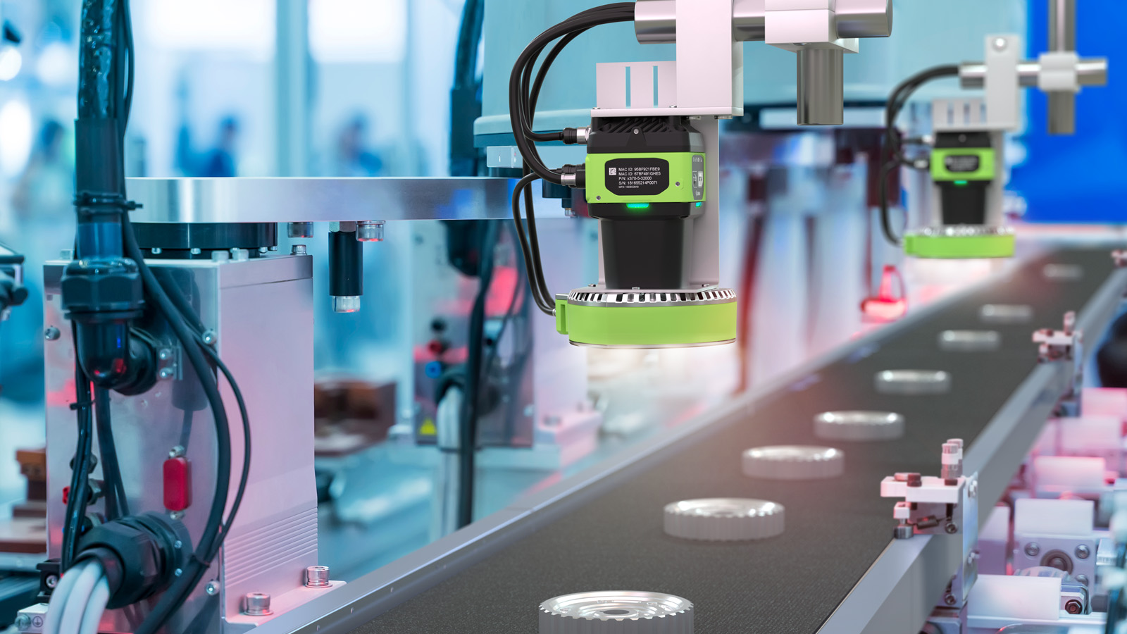 In an industrial manufacturing facility, smart cameras positioned at a conveyor belt inspect metal gears, using advanced algorithms to ensure quality by detecting imperfections in real-time as the gears pass beneath their lenses.
