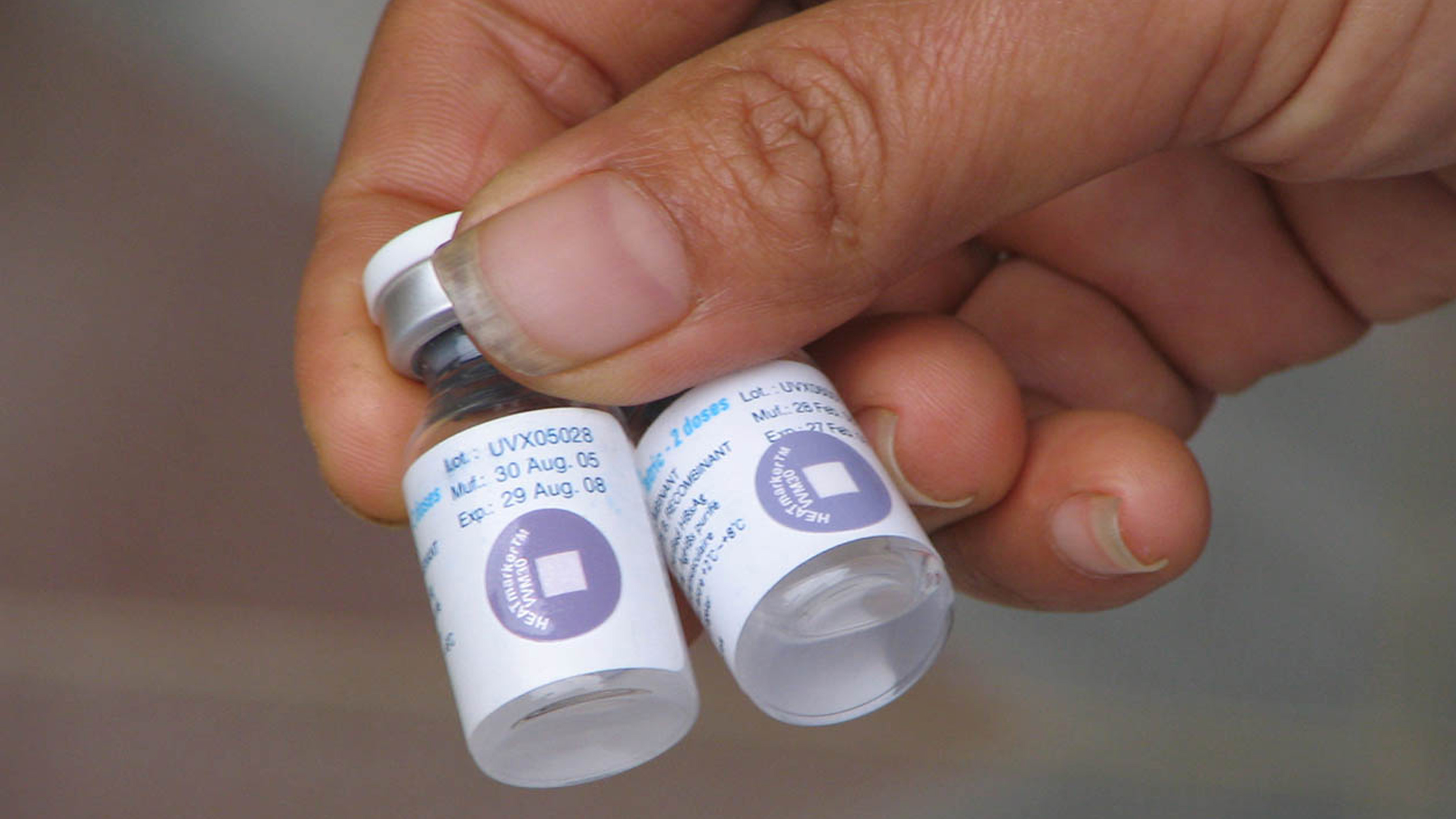 A healthcare worker holding two vaccine vials with vial monitors.