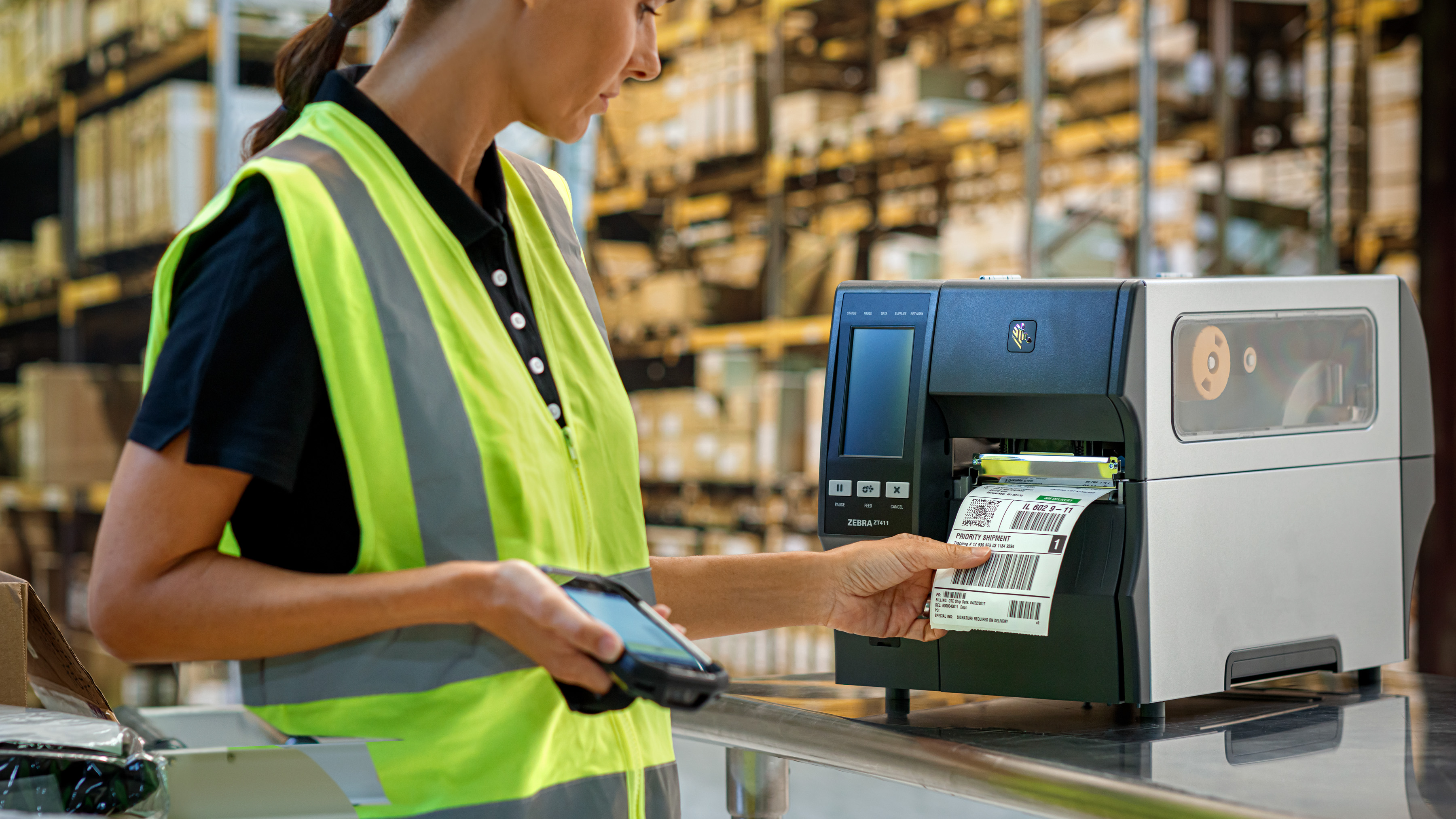 A warehouse employee printing a barcode label from a Zebra printer while holding a Zebra mobile computer.