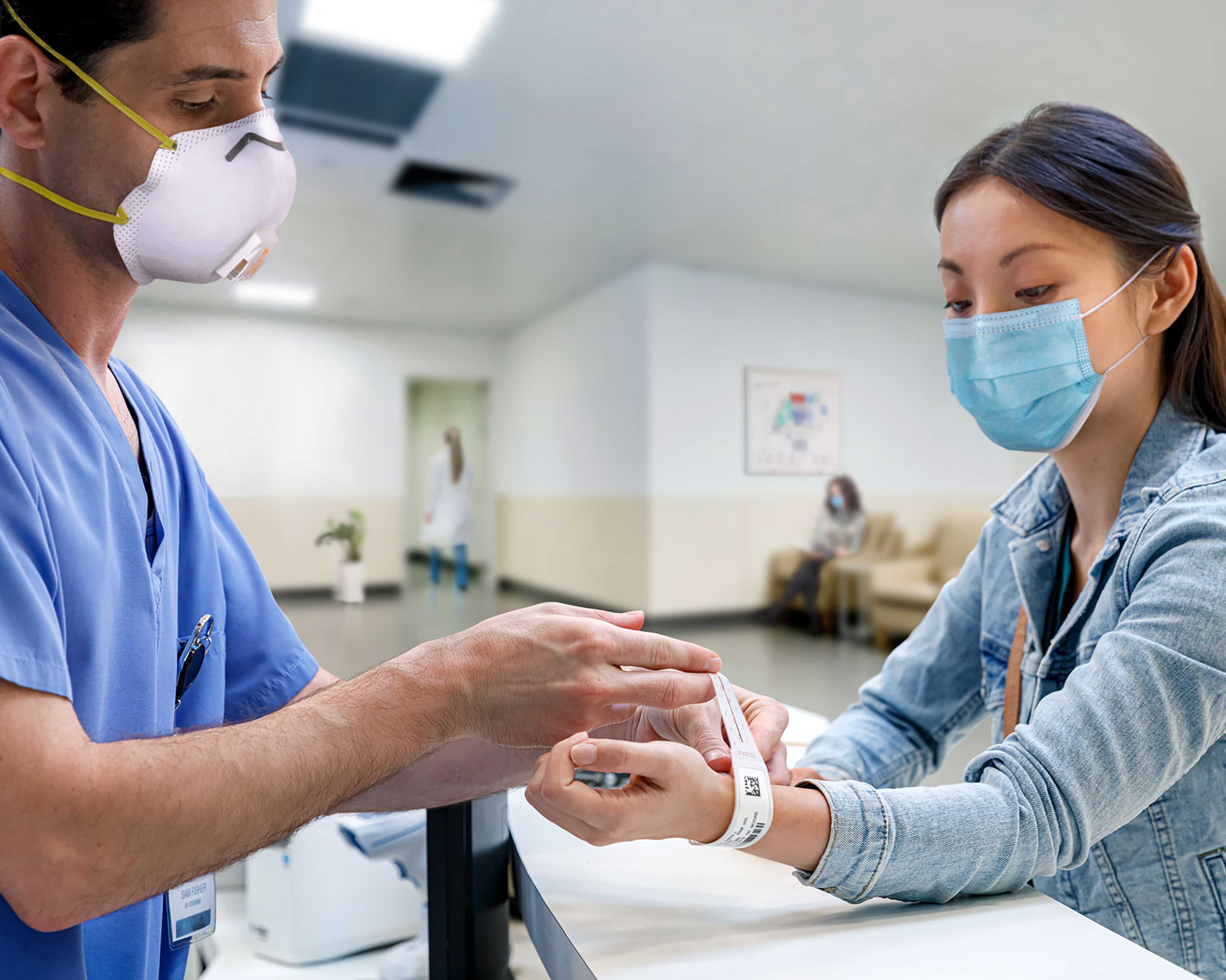 Masked nurse putting an admissions wristband on a patient's hand