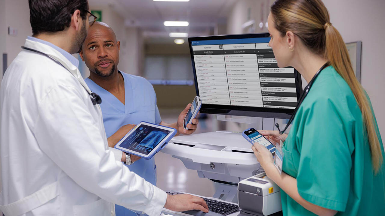 Two doctors and a nurse consult on patient while reviewing imaging and lab results on a Zebra tablet and WOW screen.