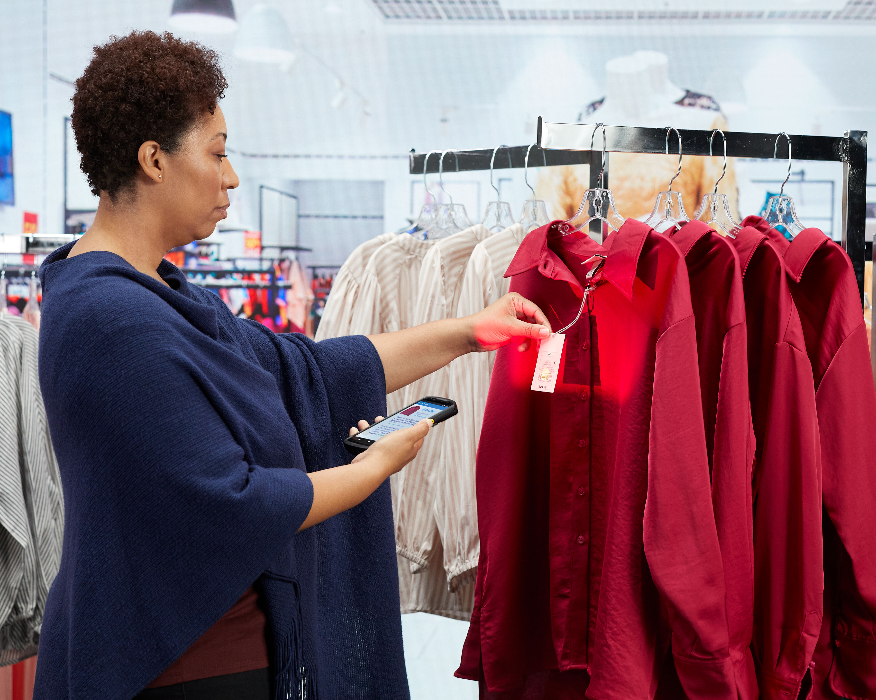 Retail worker scanning the tag on a row of red blouses