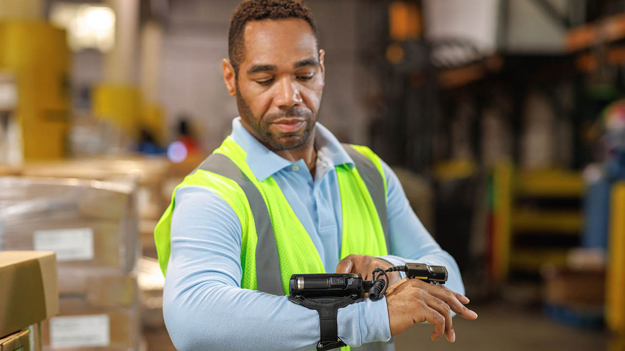 A warehouse worker looks at his wearable mobile computer after capturing data via the connected RS6100 wearable Bluetooth scanner.